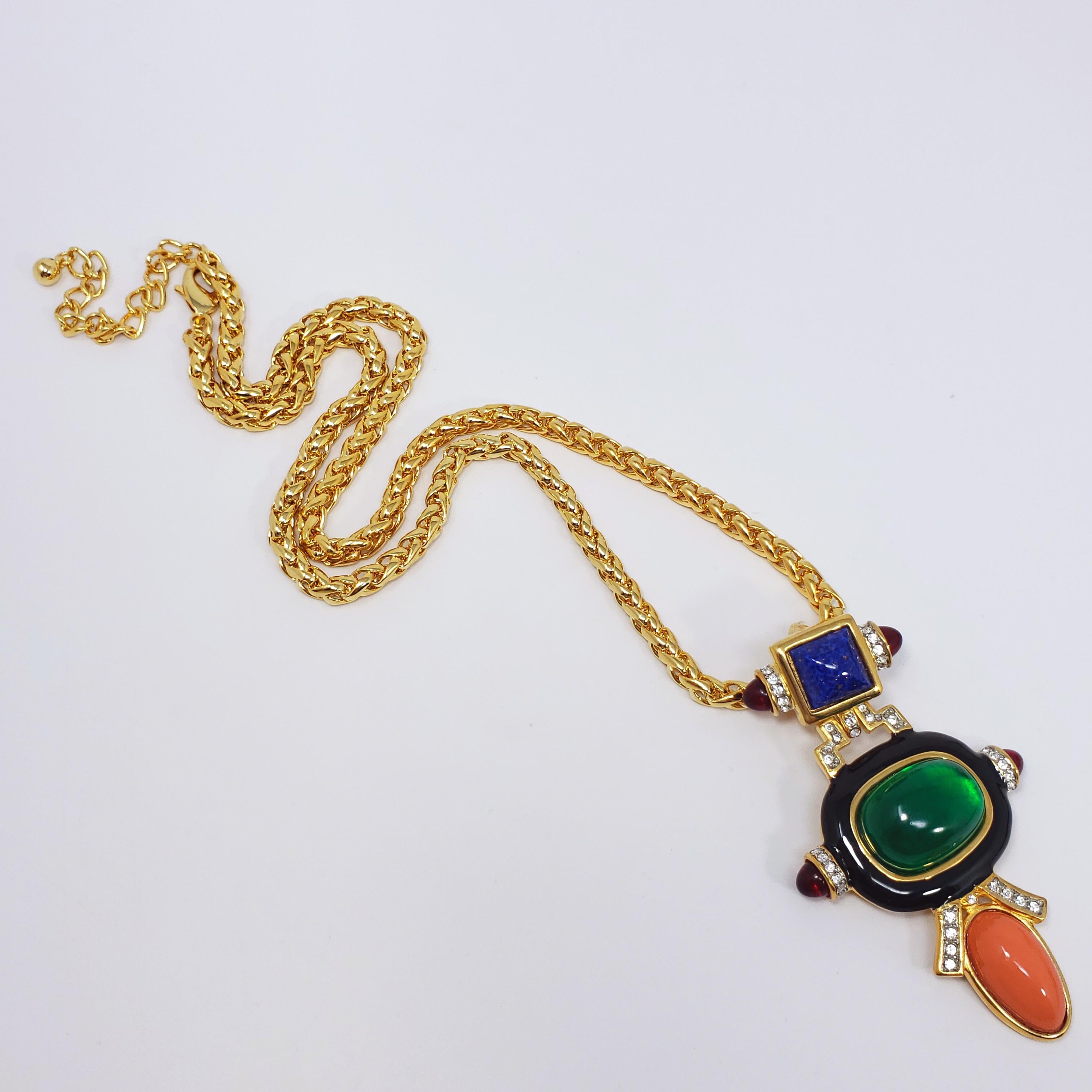 A luxurious pendant necklace from Kenneth Jay Lane's art deco line. A bold 2-piece art deco motif hangs off a thick goldtone chain, featuring faux lapis lazuli, emerald, ruby, and coral cabochons accented with black enamel and clear