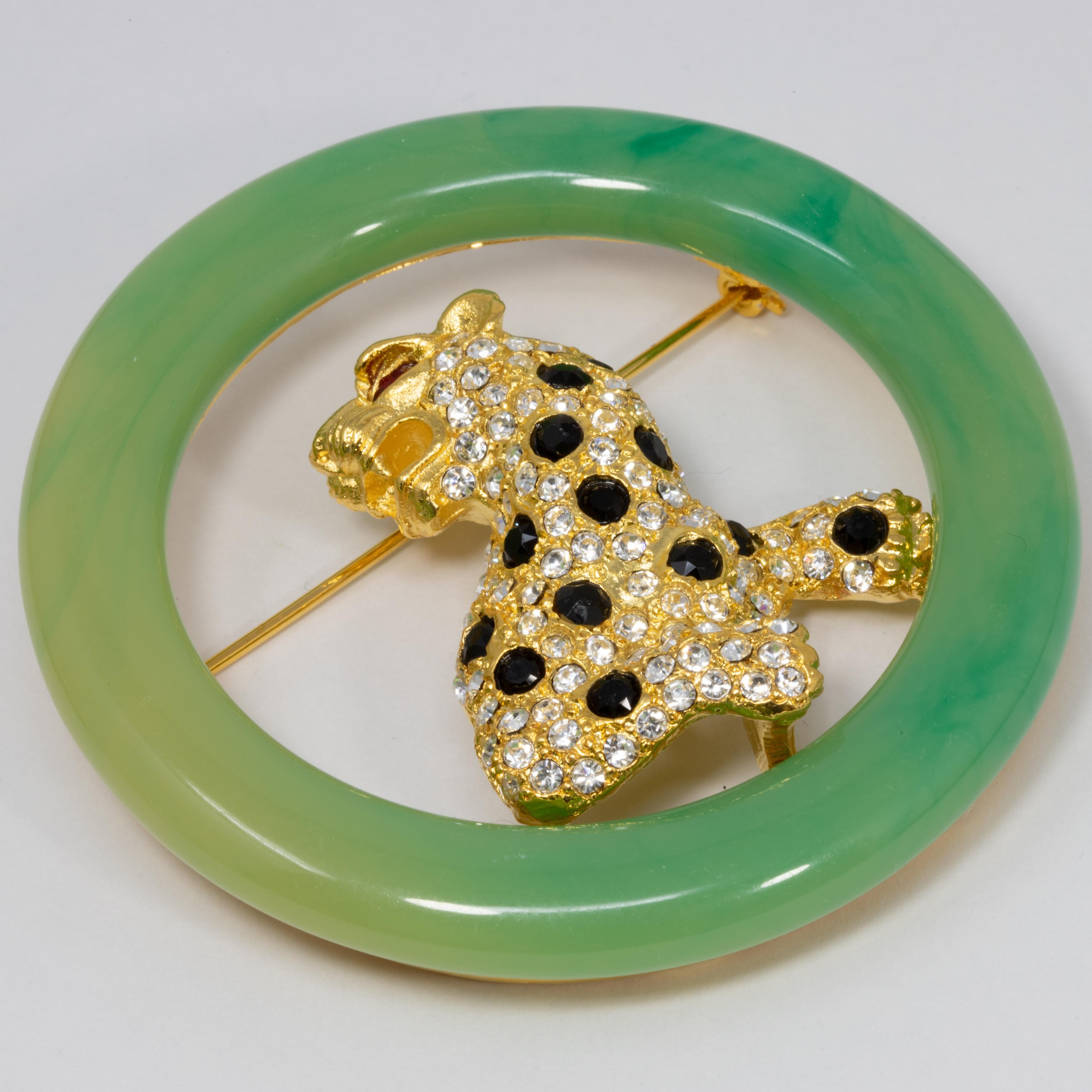 An art deco inspired pin brooch by Kenneth Jay Lane. Features a jeweled leopard cat decorated with clear, black, and red crystals in a round faux-jade frame.

Hallmarks: Kenneth © Lane, Made in USA