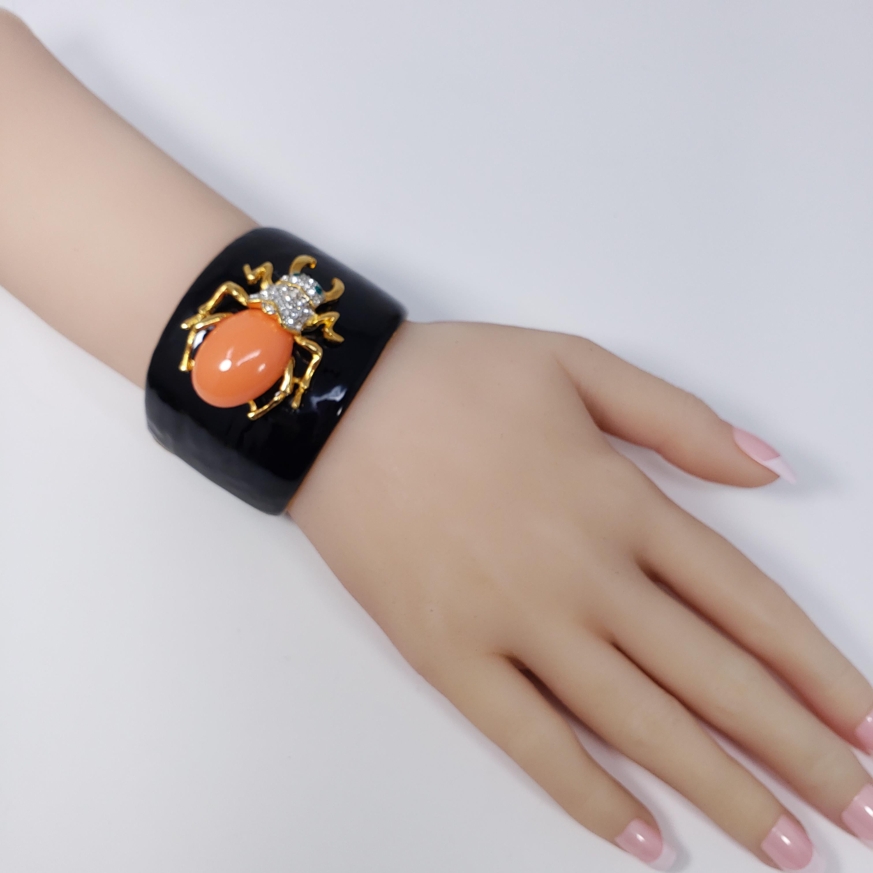 A bold cuff bracelet by Kenneth Jay Lane. Features a painted enamel front with a decorated scarab motif. The bug features a coral-colored resin cabochon back and white and green pave crystals. A stylish accessory!

Hallmarks: KJL
Inner