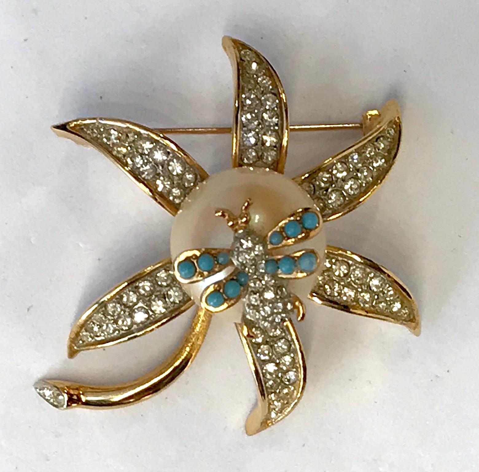 Three dimensional flower by Kenneth Jay Lane prior to 1973. Gold tone with petals in pave' rhinestones. In the center is set a large 19 mm faux pearl. Atop of the pearl is mounted a .62 x .75 of an inch bee with rhinestone body and turquoise color