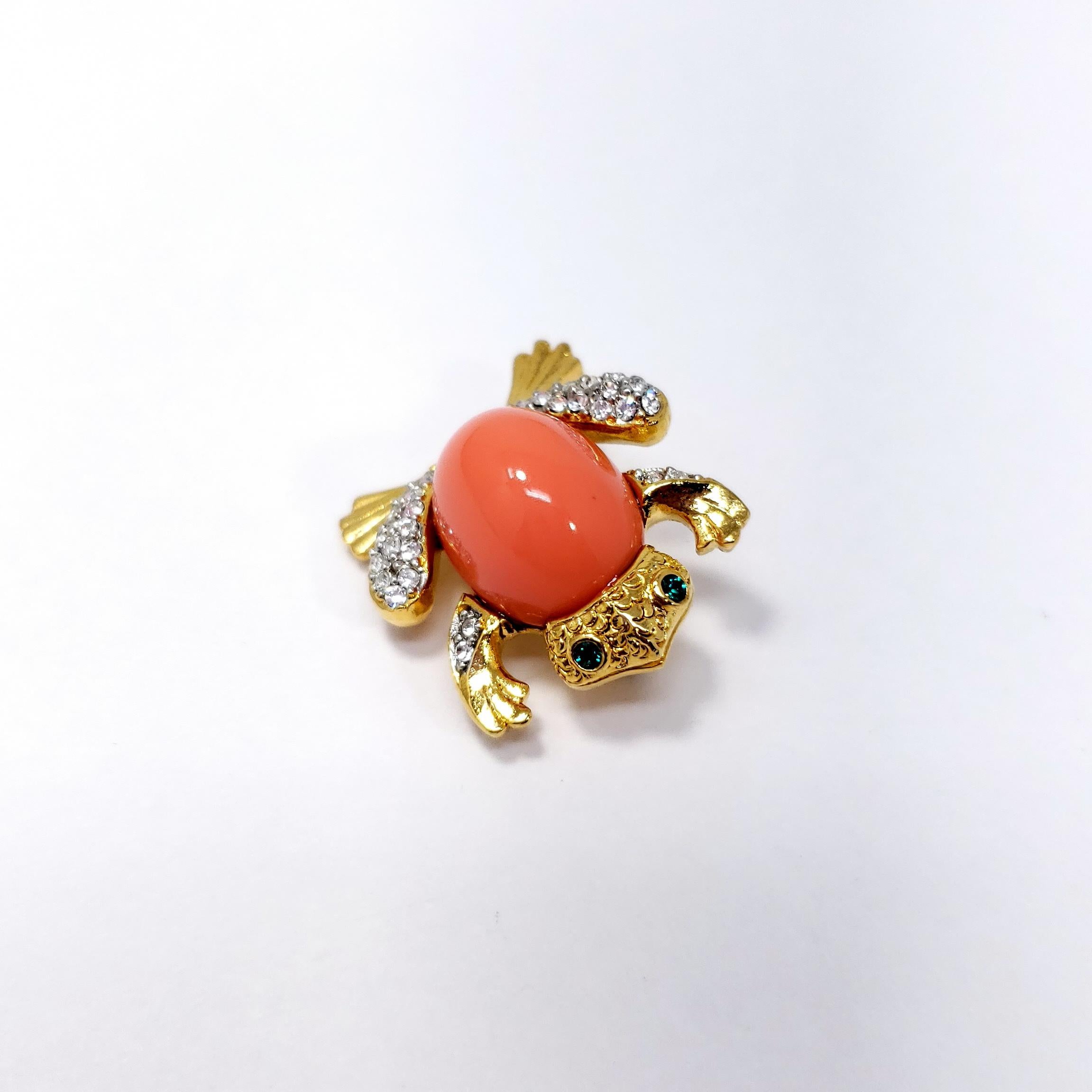 Whimsical Kenneth Jay Lane frog brooch, featuring a faux coral cabochon accented with clear and green crystals. Gold plated.

Hallmarks: Kenneth Lane