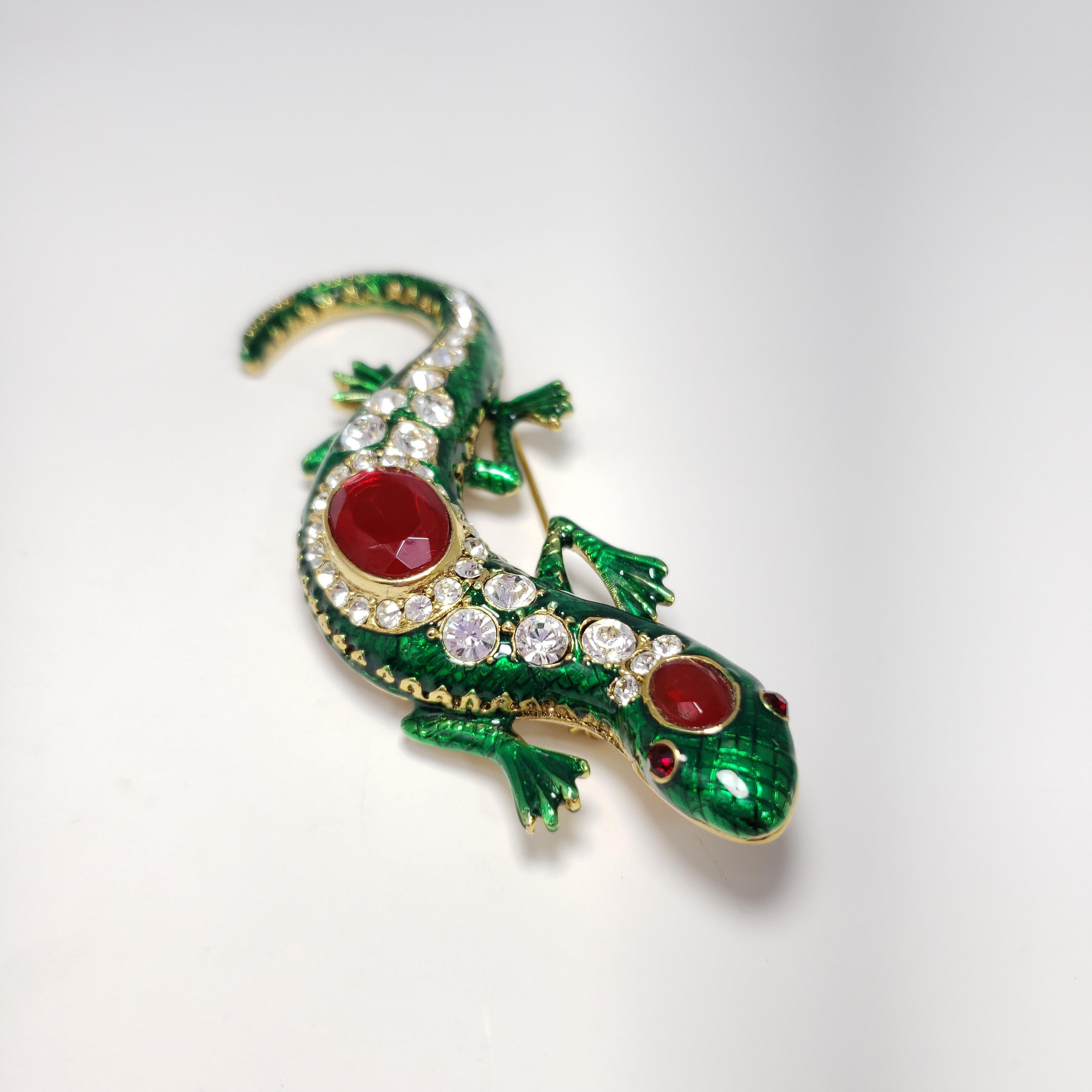 A colorful pin/brooch by Kenneth Jay Lane. This green salamander is decorated with glittering clear and ruby crystal. Gold-plated metal.

Hallmarks: Kenneth © Lane