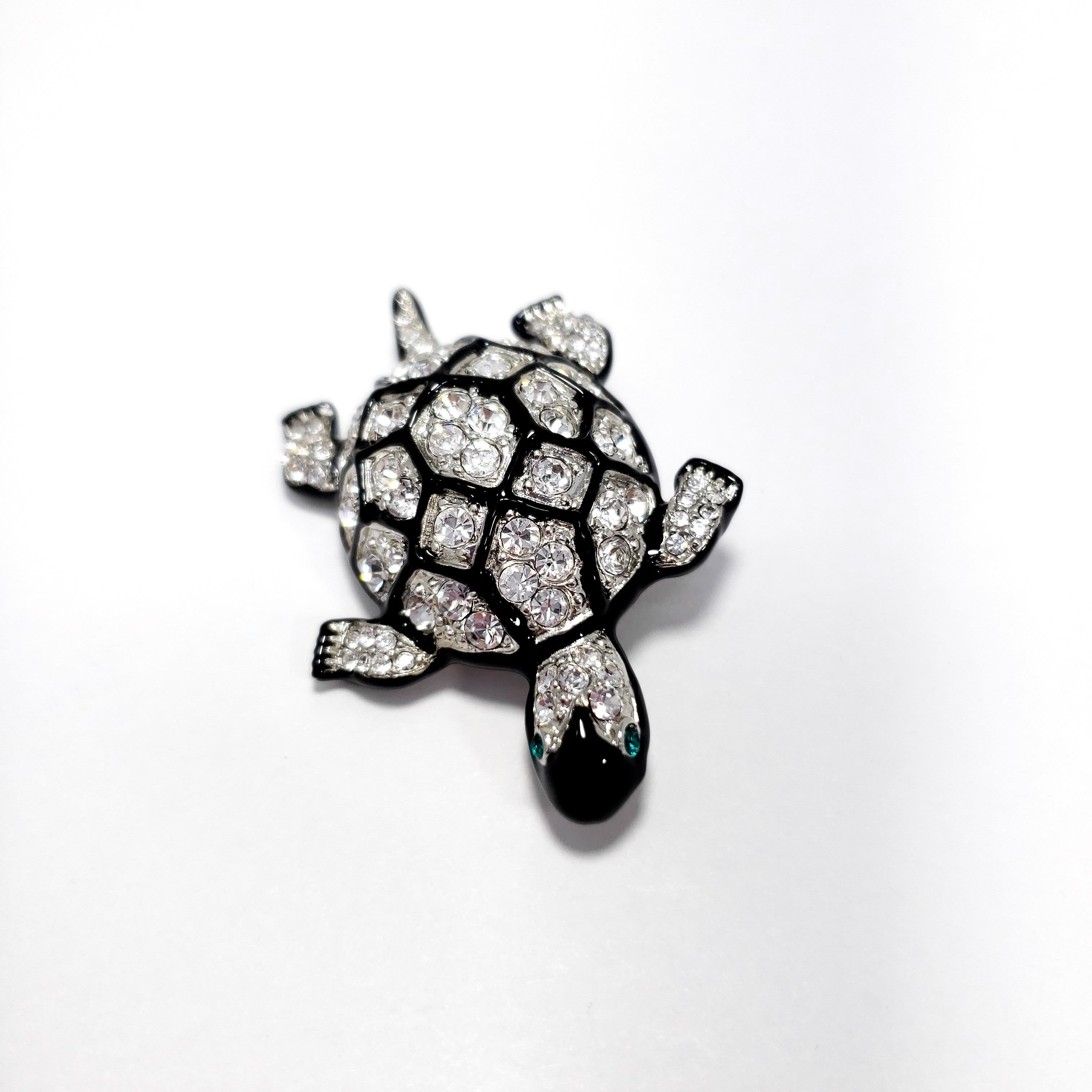Eine Brosche von Kenneth Jay Lane. Diese funkelnde Schildkröte ist mit klaren Pave-Kristallen besetzt, die mit schwarzen Emaille-Konturen auf dem Panzer akzentuiert sind.

Punzierungen: Kenneth Lane, Hergestellt in den USA