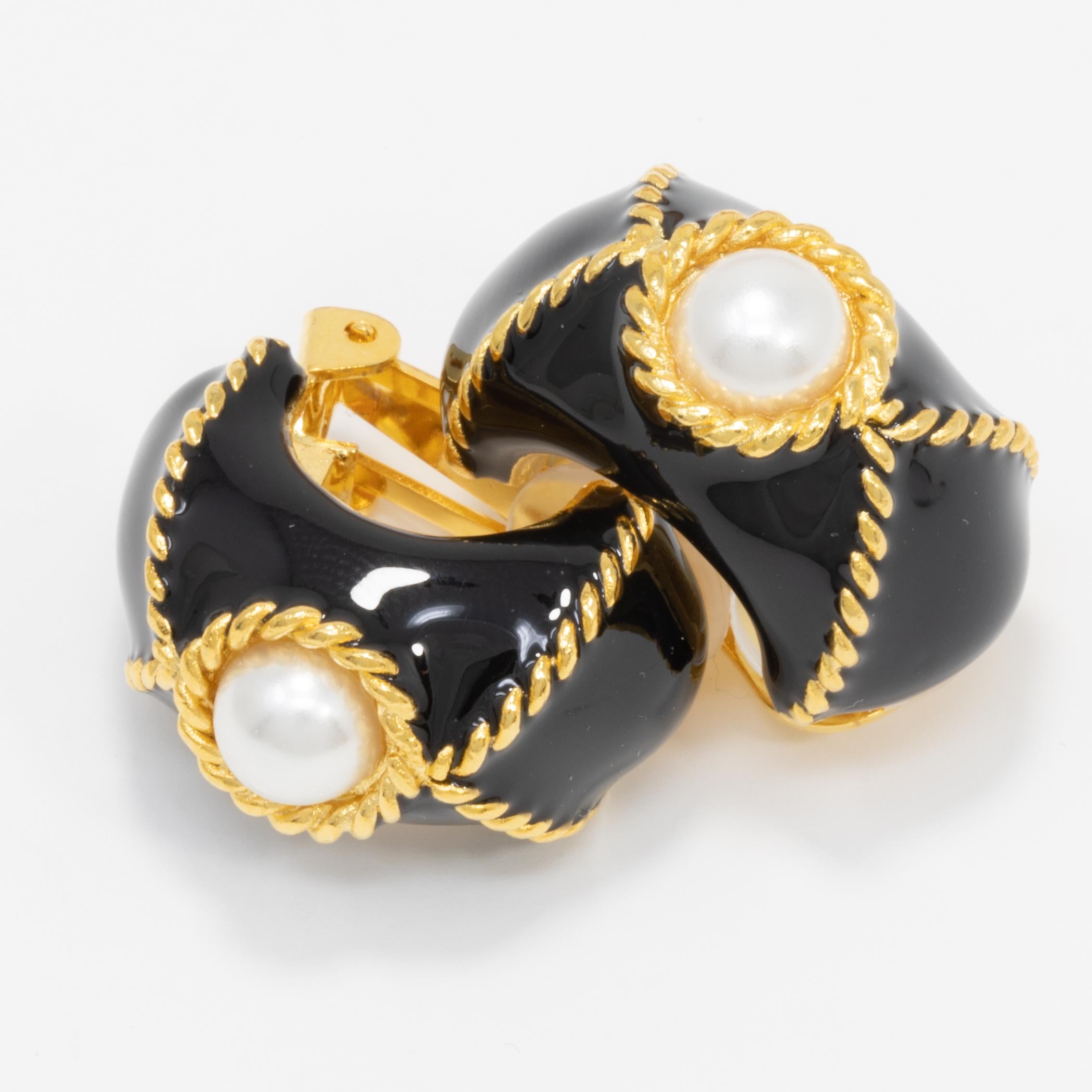 A pair of clip on earrings by Kenneth Jay Lane. Each gold-plated earrings is painted in black enamel, and decorated with a faux pearl centerpiece and gold accents.

Tags, Marks, Hallmarks: KJL, Made in USA