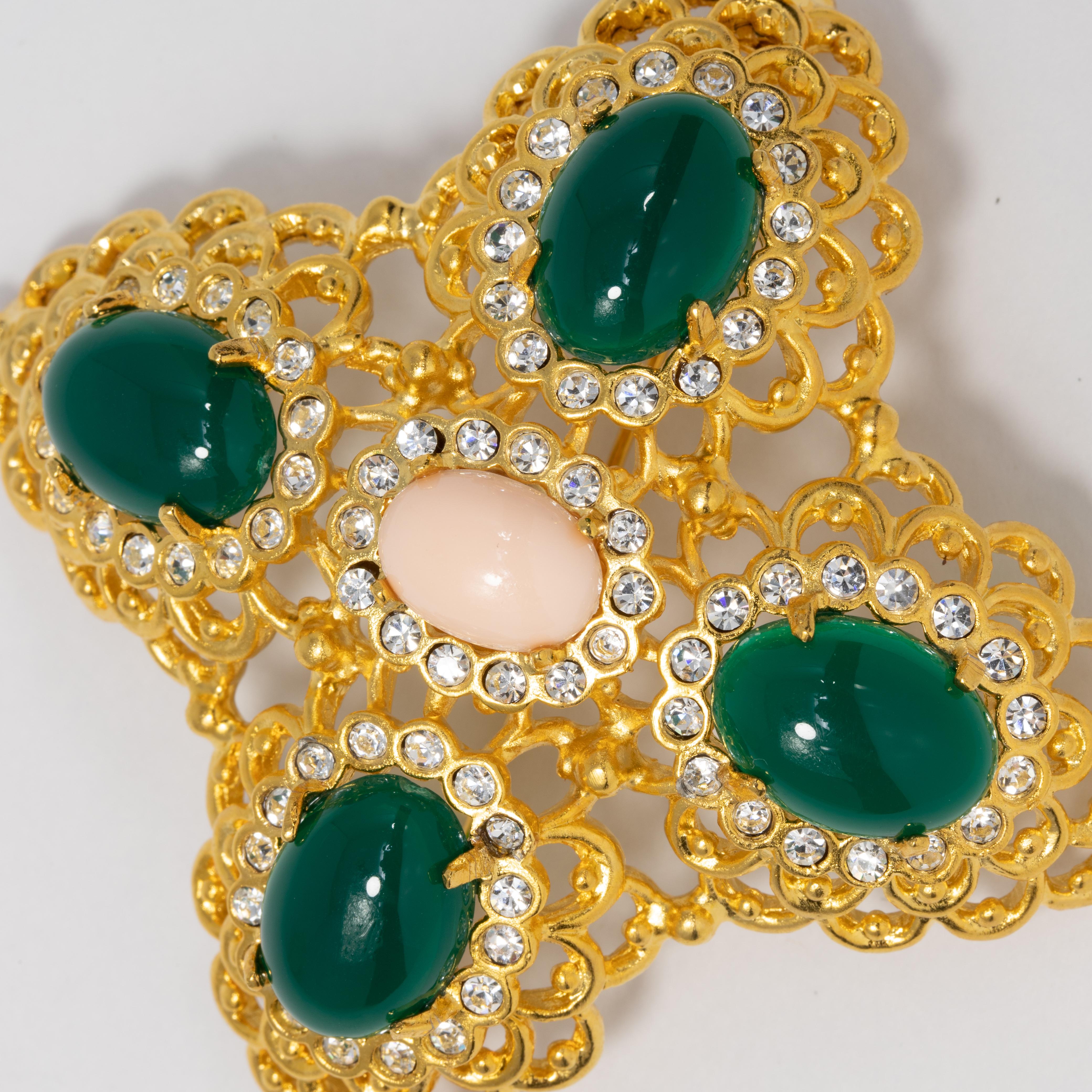 A stylish pin by Kenneth Jay Lane featuring prong-set green and pink cabochons, accented with clear crystals and set in a decorative filigree goldtone setting.

Hallmarks: Kenneth Lane