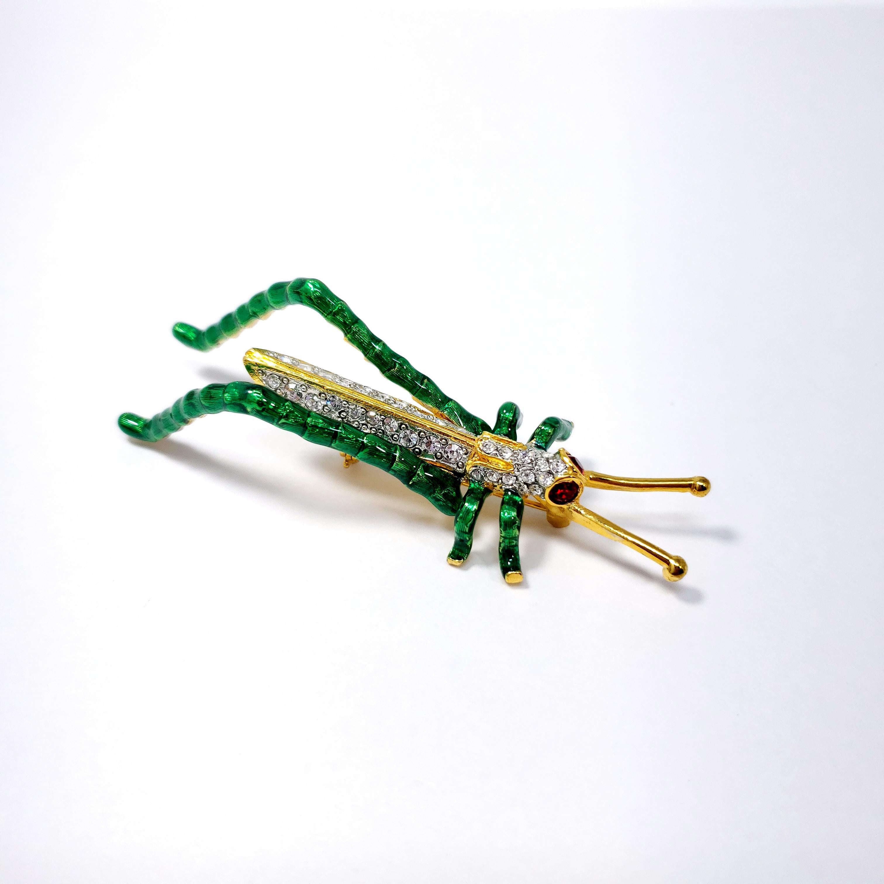 Clear and ruby crystals decorate this whimsical grasshopper pin brooch by Kenneth Jay Lane.

Painted green enamel on gold plated metal.

Hallmarks: KJL