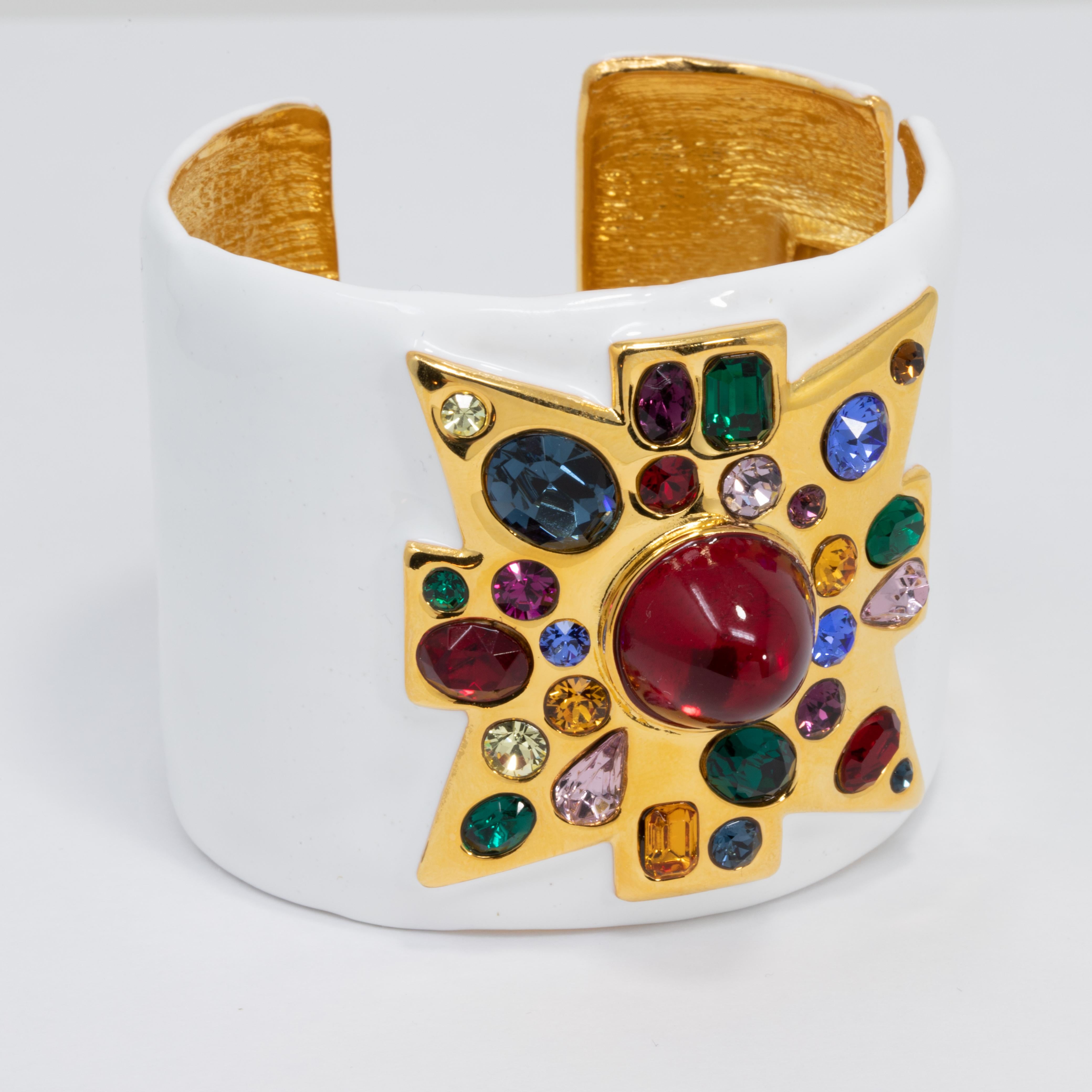 A stylish Kenneth Jay Lane cuff bracelet. Features a gold-plated cuff painted in white enamel. A bold maltese cross motif is accented with colorful crystals and a vibrant centerpiece red cabochon.

Hallmarks: KJL, Made in USA
Inner circumference: 3