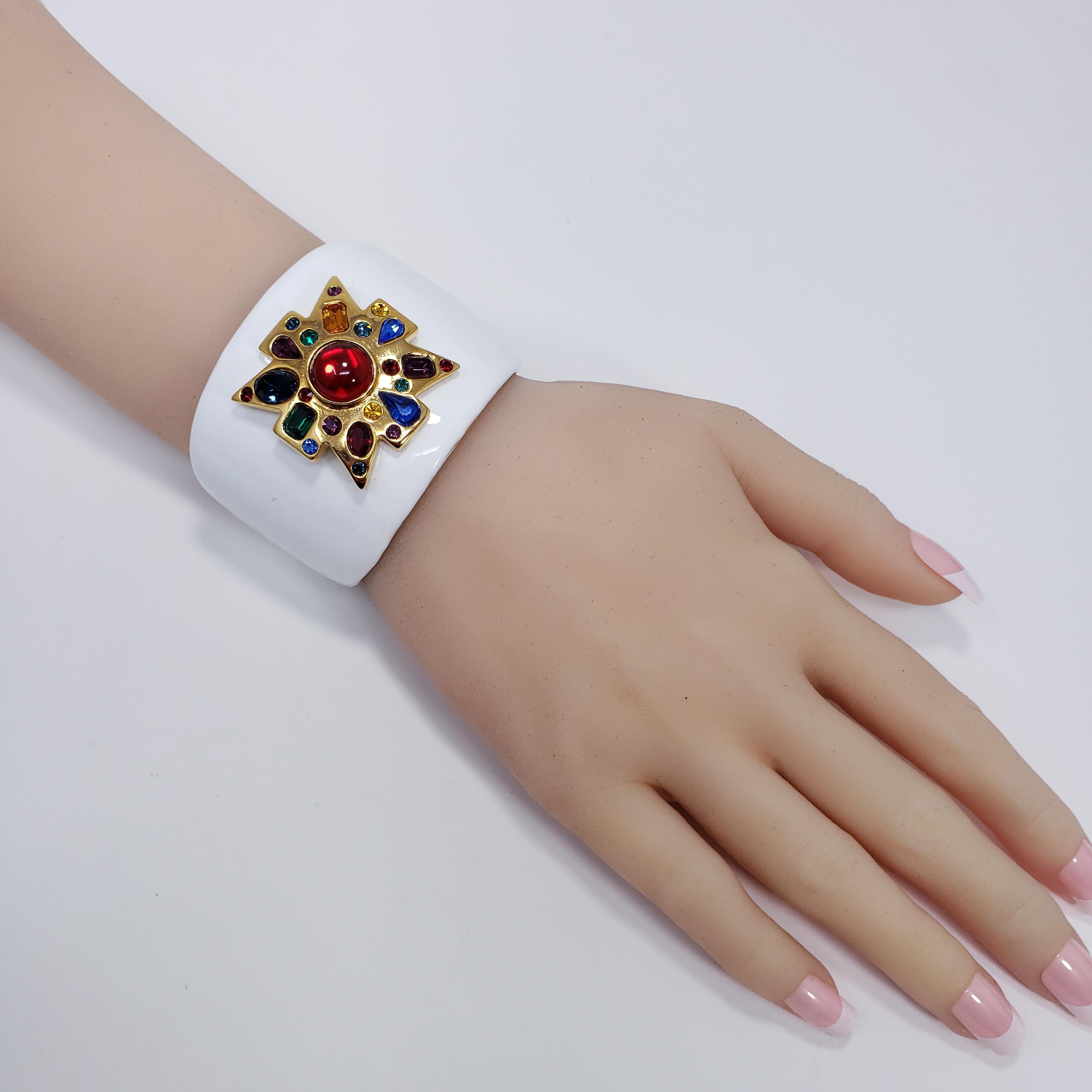 A stylish Kenneth Jay Lane cuff bracelet. Features a gold-plated tapered band painted in white enamel. A bold maltese cross motif is accented with colorful crystals and a vibrant centerpiece red cabochon.

Hallmarks: KJL
Inner circumference: 15