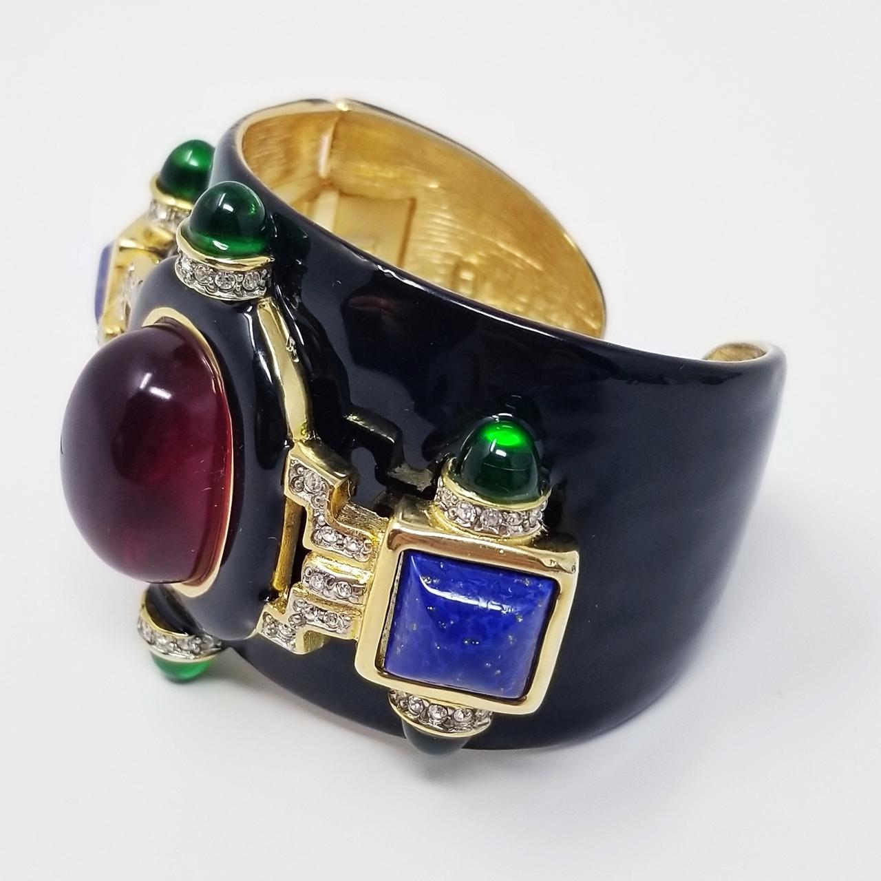 Kenneth Jay Lane cuff bracelet. Black enamel and 22KT gold plated. Ruby resin cabochon centerpiece accented with faux emerald, lapis lazuli, and clear crystals.

...

Measurements: inner circumference 6