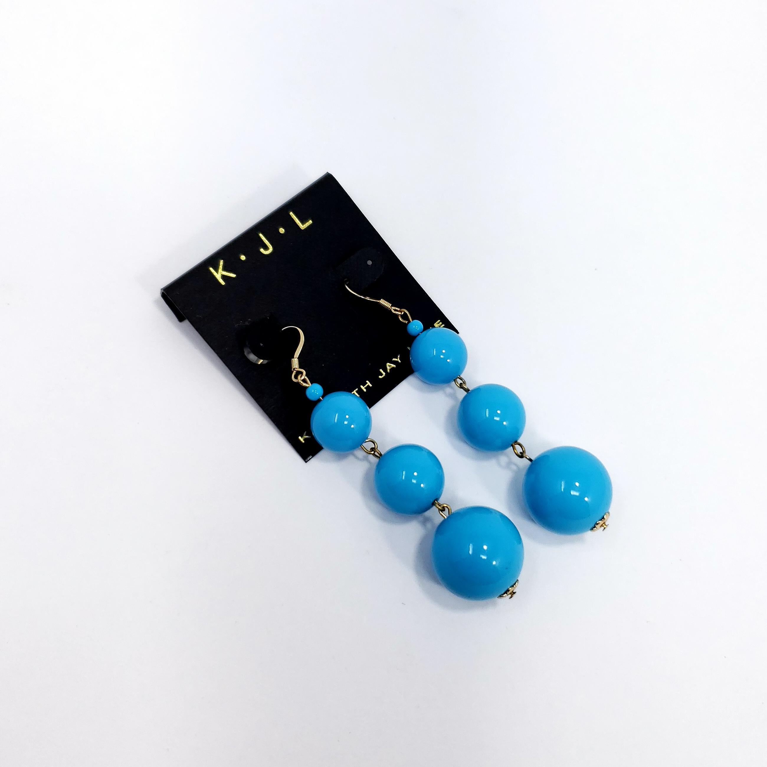 A pair of bright blue turquoise earrings. Three turquoise-blue graduated beads dangle from gold-plated hooks. By Kenneth Jay Lane.

8cm drop. Largest bead is 2cm large. 

Hallmarks: none