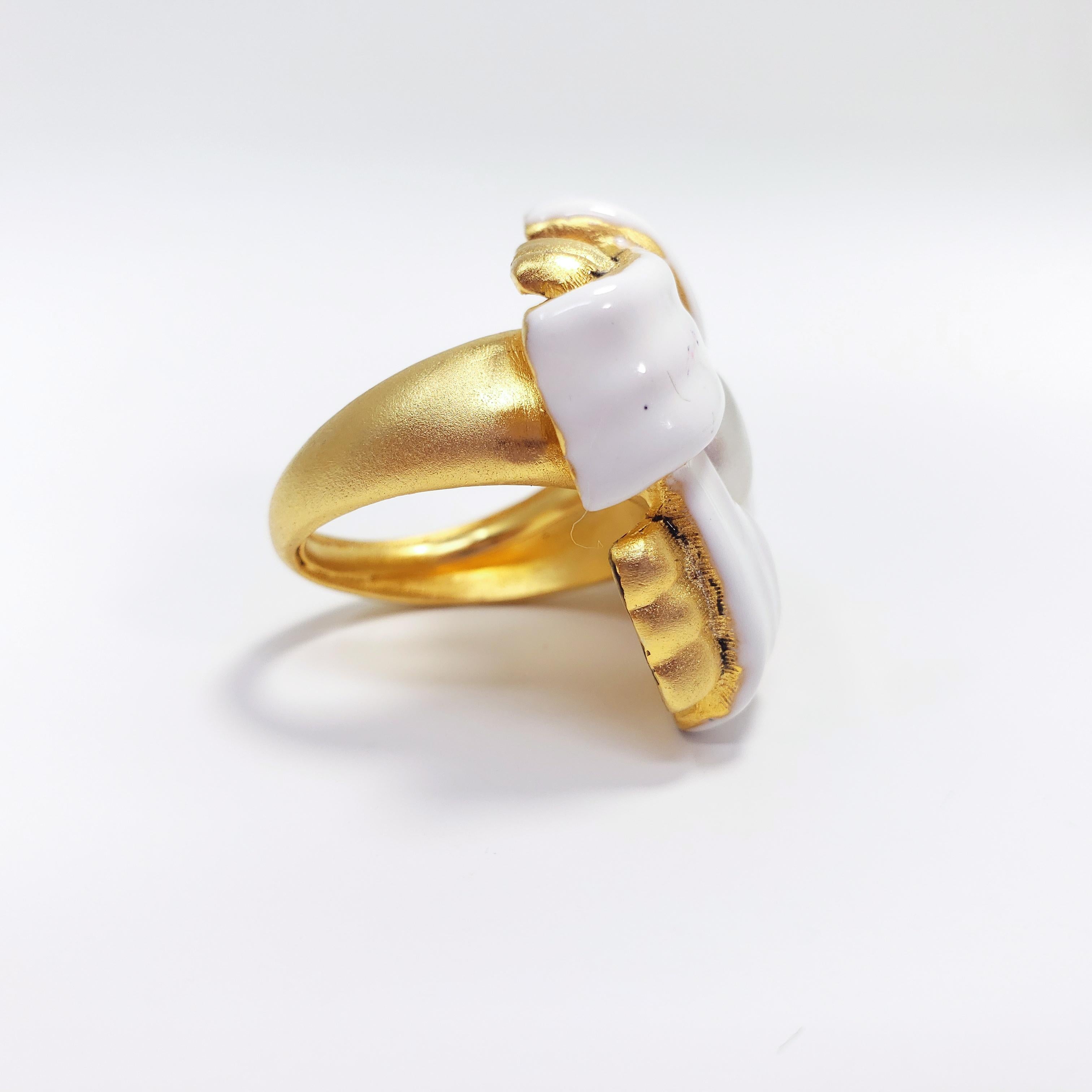 A goldtone Kenneth Jay Lane cocktail ring featuring intertwined ribbon motifs painted with white enamel, accented with a centerpiece faux pearl.

Size: Adjustable, US sizes 4-8
Face height 3.2 cm
Hallmarks: Kenneth © Lane