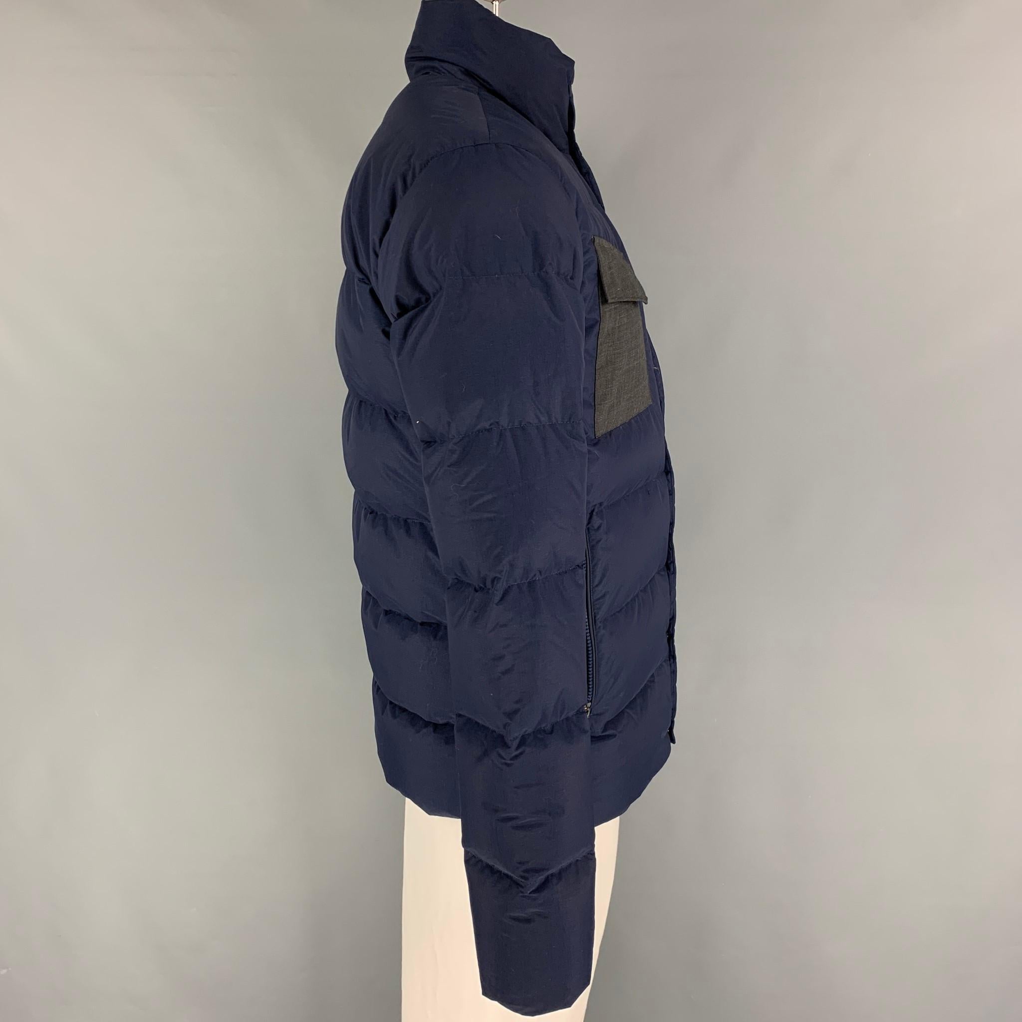 KJUS jacket comes in a navy & grey quilted polyamide with premium down fill featuring a high collar, patch pockets, sleeve logo detail, and a snap button closure. 

Excellent Pre-Owned Condition.
Marked: 50/M

Measurements:

Shoulder: 19 in.
Chest: