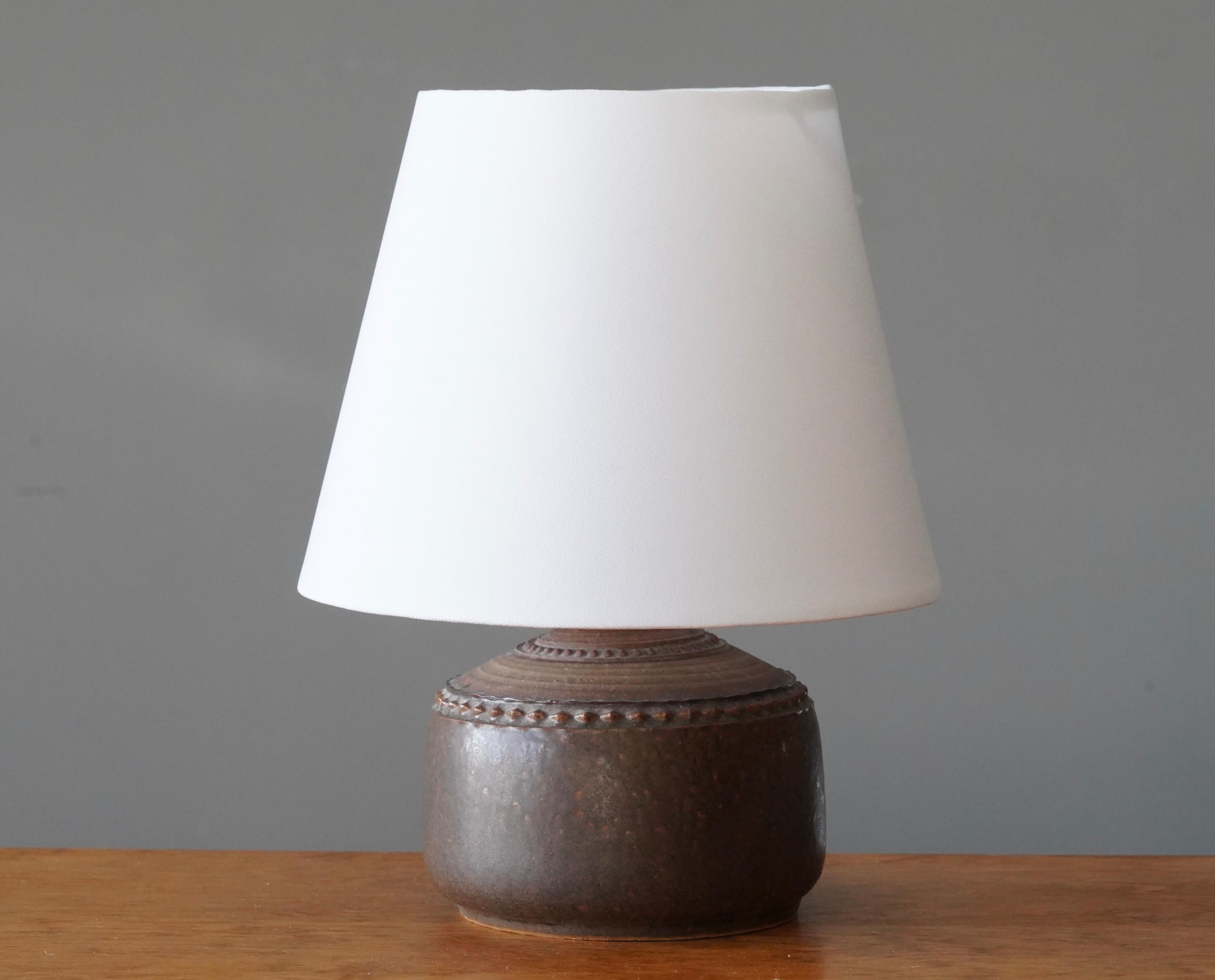 A table lamp by Klase Höganäs. In stoneware with simple incised decor. Signed. 

Dimensions listed are without lampshade. 
Dimensions with shade: height is 10.5 inches, width is 8.25 inches.
Dimensions of shade: top diameter is 5.25 inches,