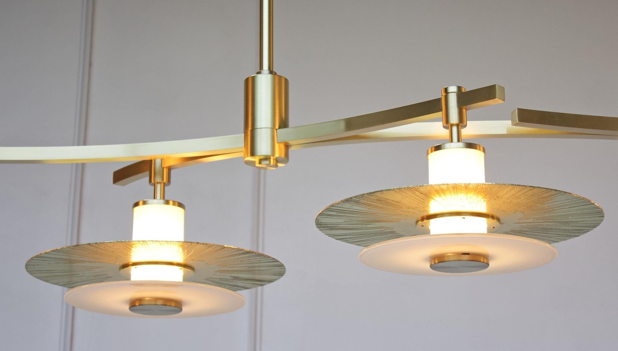 The Klein Chandelier embraces a linear series of layered light assemblies comprising hand blown glass rondelles and etched and polished brass discs. Mounted to a central white light tube, the Klein Chandelier offers ample up lighting as well as a