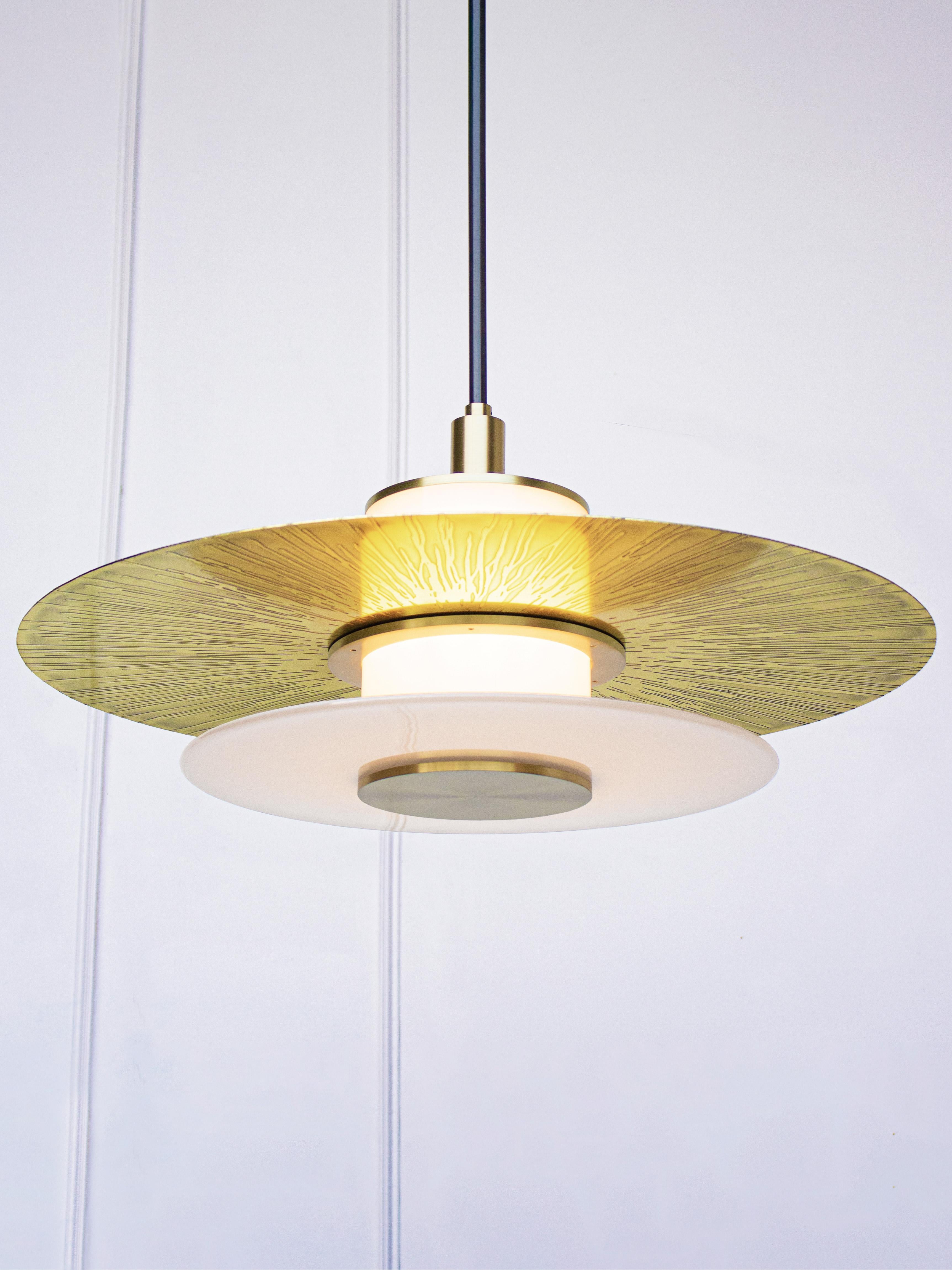 At 24 inches in diameter the Klein Pendant embraces a layered light assembly comprising a hand blown glass rondelle and an etched and polished brass disc. Mounted to a central white light tube, the Klein Pendant offers ample up lighting as well as a