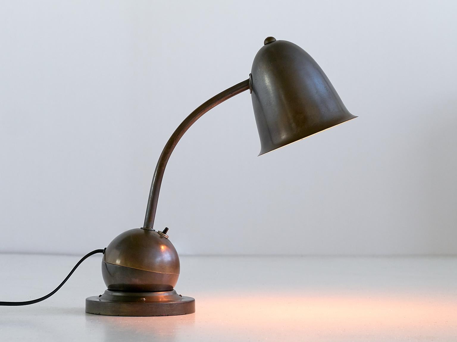 This rare desk or table lamp is called The Tumbler (De Tuimelaar) and was produced by KMD Daalderop in the Netherlands, circa 1935. The striking design in bronzed metal is marked by the elegant bell shaped shade and the curved stem. The shade can be