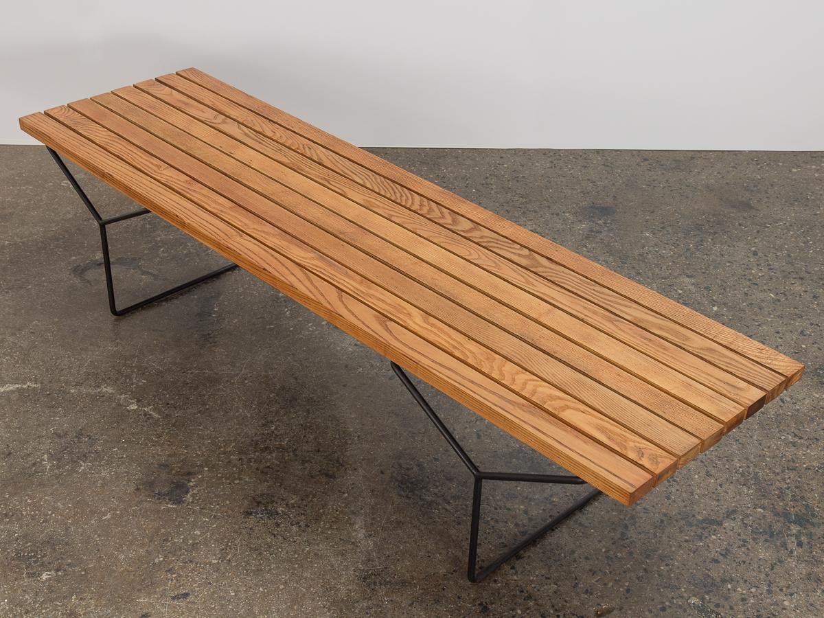 An early edition of the iconic model 400 slatted bench, designed by Harry Bertoia for Knoll. A minimal form, comprised of solid oak slats balanced on Y-shaped legs. Contrasting black metal supports hint at the sculptural signature of the designer's