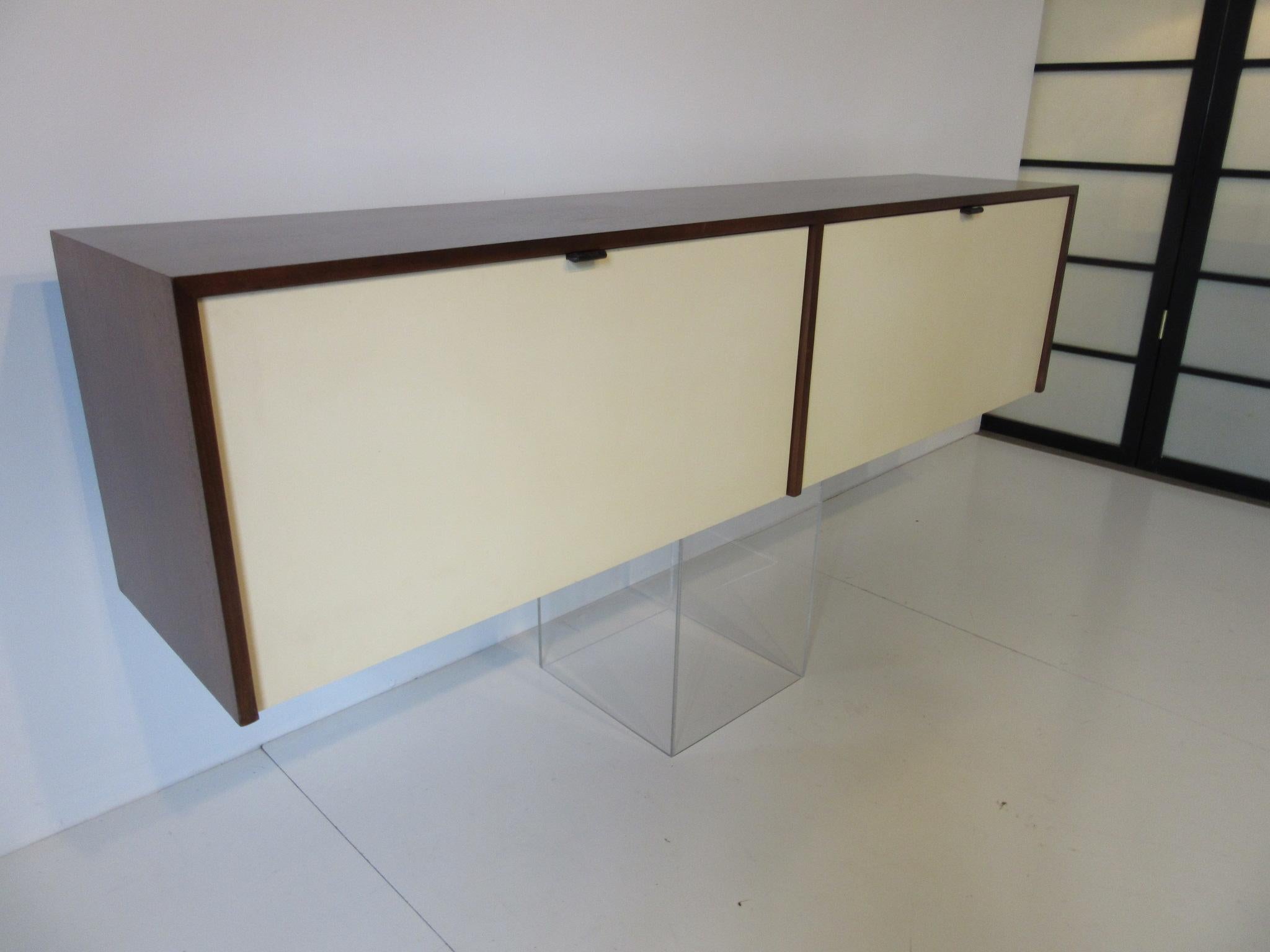 A dark walnut hanging credenza cabinet with double doors, black leather pulls, three adjustable shelves to the right side and two smaller adjustable glass half shelves to the other side. Retains a partial manufactures label to the bottom from Knoll.