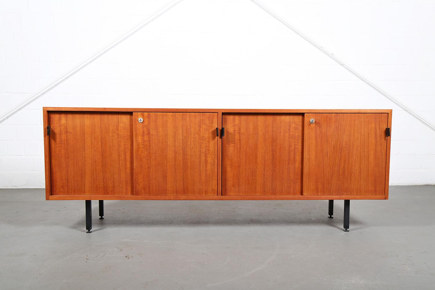 Knoll International teak sideboard designed by Florence Knoll in the 1950s including the typical, beautiful door handles made of black thick leather. Inside with lighter wood and adjustable shelves. Marked inside and on the back with manufacturer’s