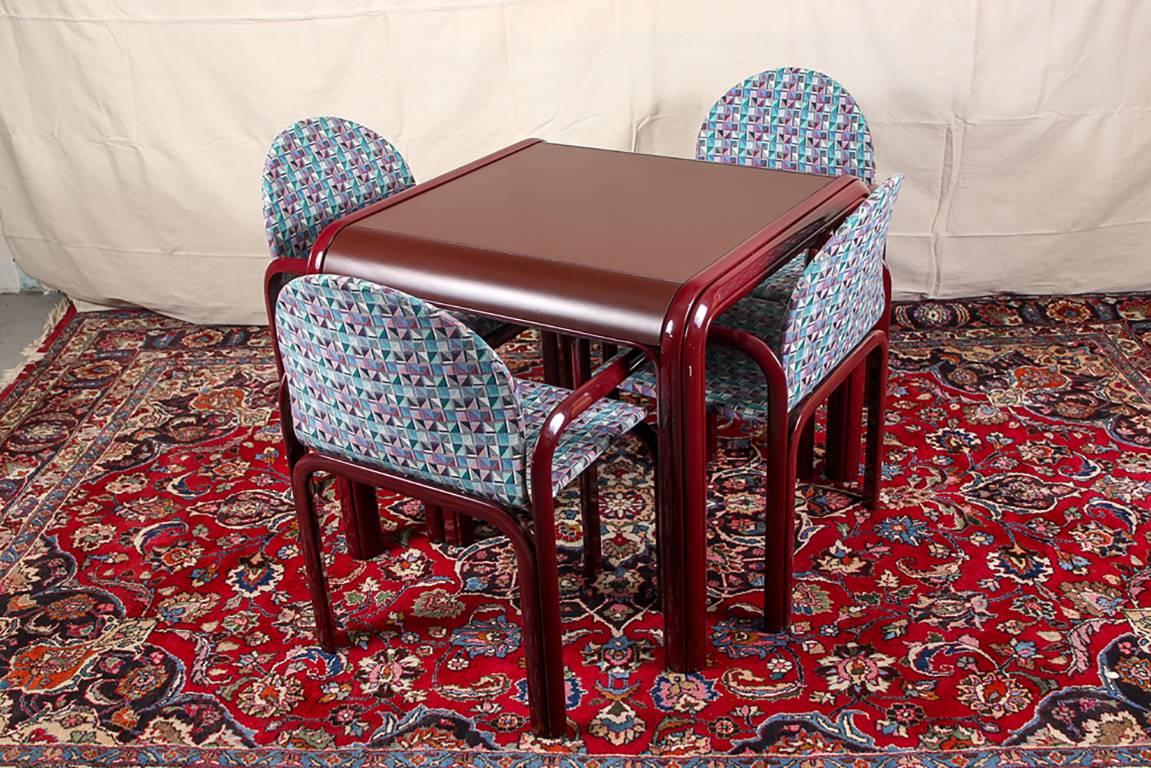 Knoll International card table and four chairs, burgundy tones with a melamine curved ended table top with lacquered triple curved side supports. Four armchairs with curved front and back frames linked to the one-piece curved arms and legs,
