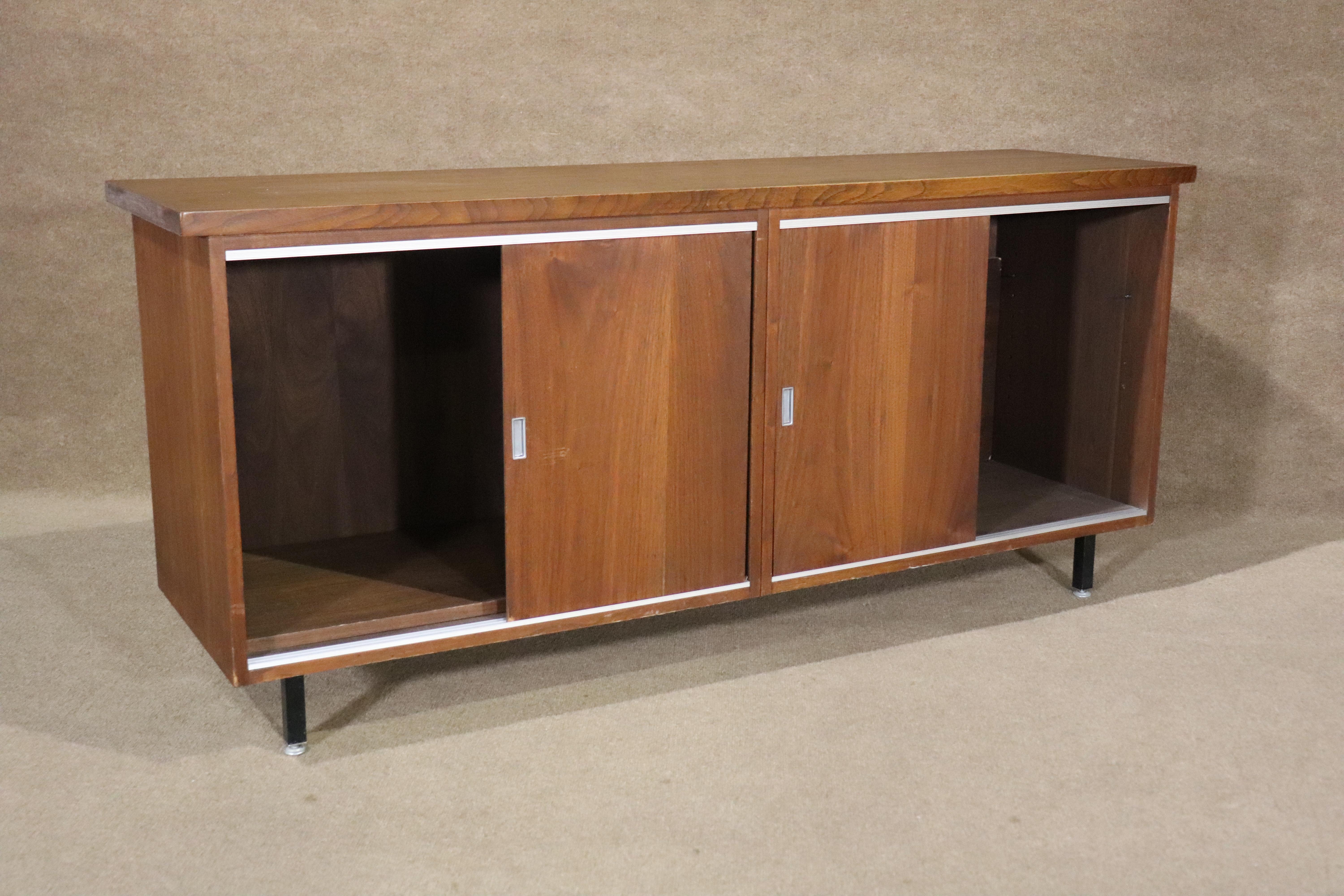 Long mid-century modern office cabinet in walnut wood grain with aluminum hardware and matching runners. Sliding doors reveal two large cabinets with shelf capability. Great for your modern home or office use.
Please confirm location NY or NJ