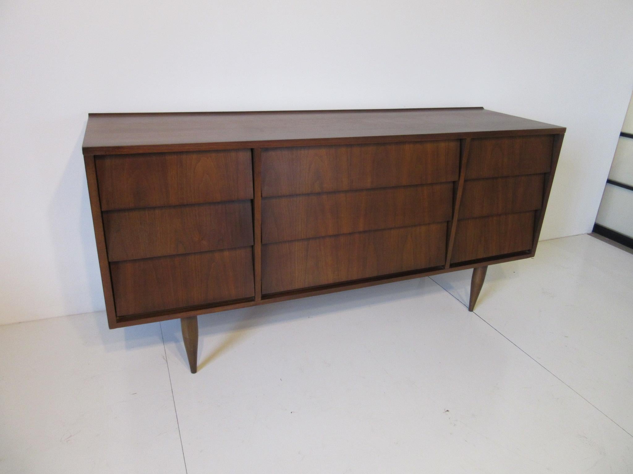 A walnut dresser chest with nine slanted drawer fronts, raised back lipped edge to the top all on conical legs in the style of Knoll.