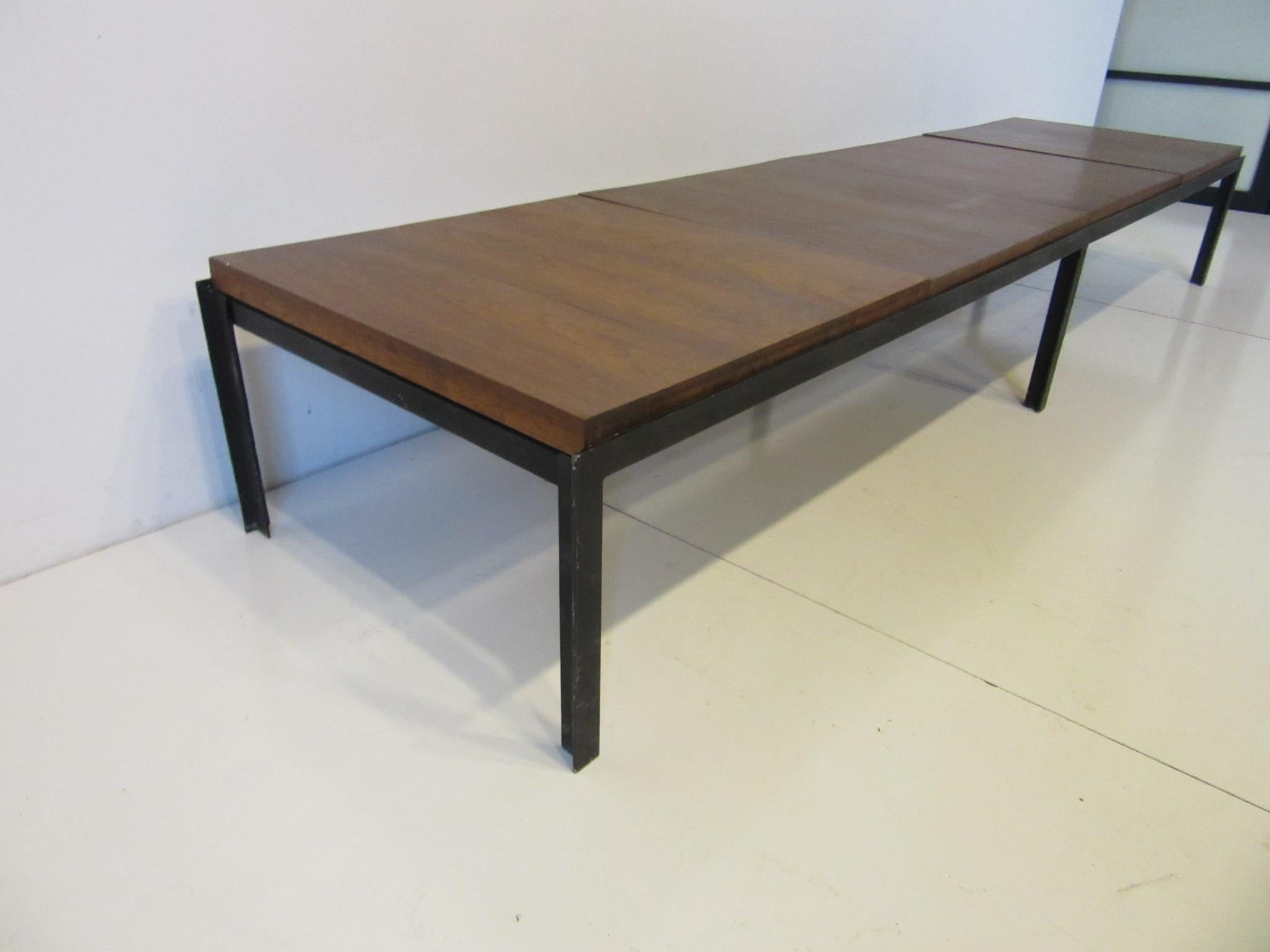 A satin black metal T - angled framed low coffee table / bench with four segmented black walnut squares , this well made piece is from the T - Angle Series designed by Florence Knoll and 
 manufactured by Knoll.