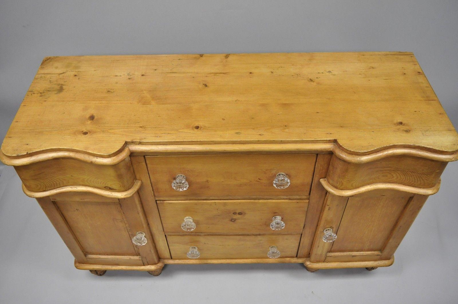 Antique knotty pinewood country primitive sideboard. Item features six turn carved bun feet, glass knobs, serpentine front, solid wood construction, distressed finish, two swing doors, five dovetailed drawers, and quality craftsmanship, circa 19th
