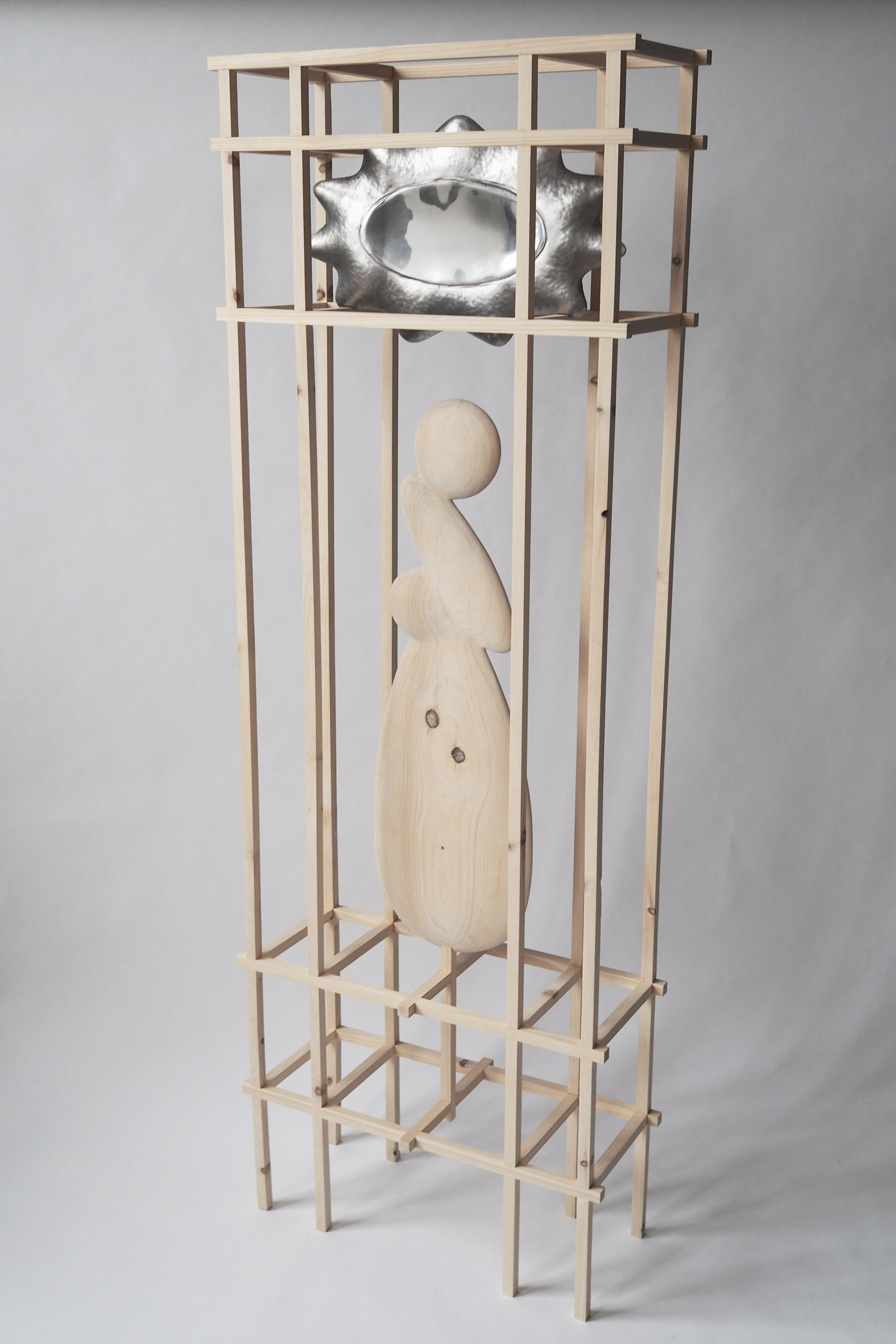 Two hammered steel shells, welded, one side polished and housed in a gridded structure of knotty pine wood. The two disparate elements are bridged by a third, a carved pine form completing the composition.