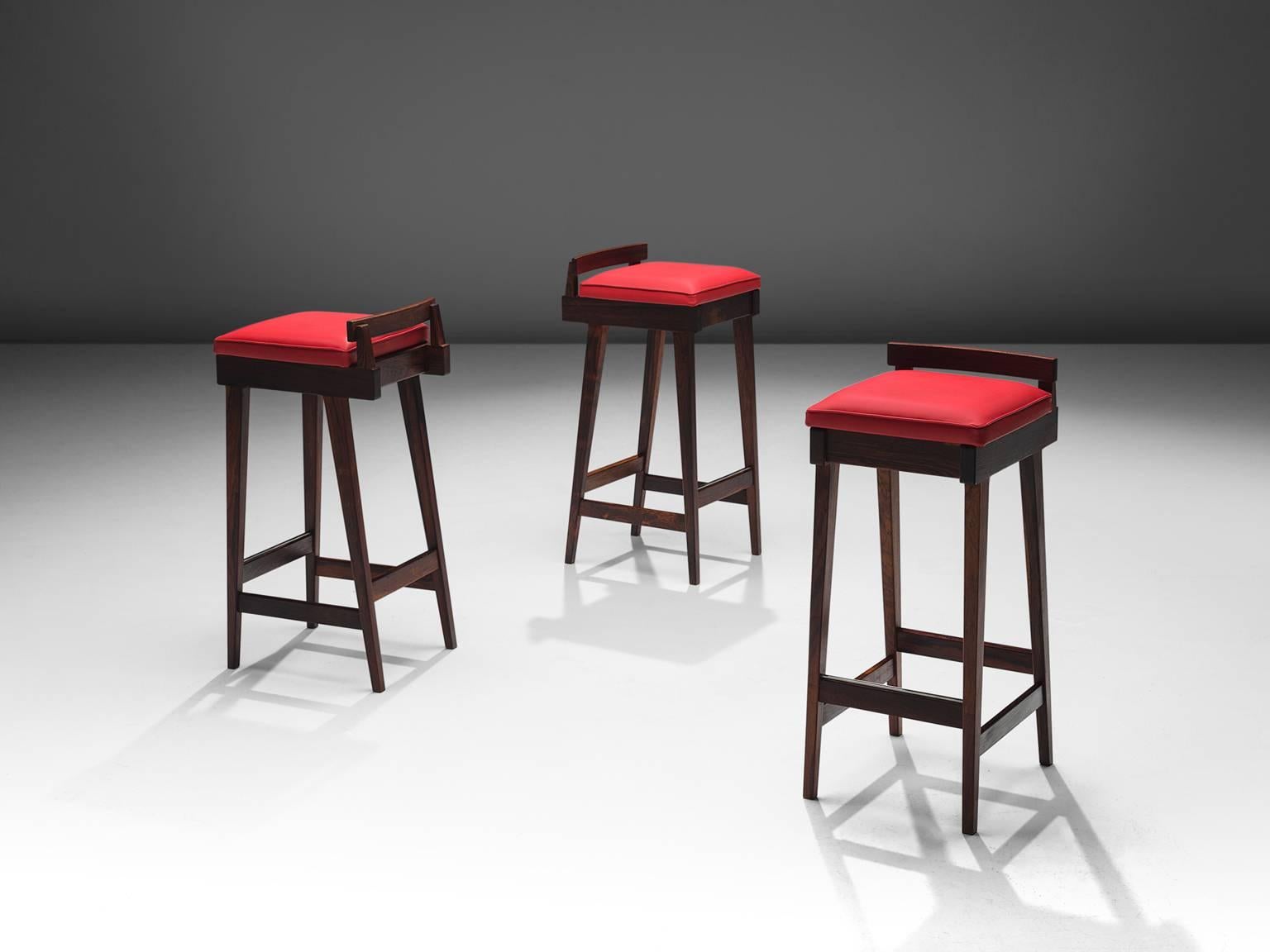 Knud Bent for Dyrlund, three bar stools, rosewood and red faux leather, Denmark, 1950s 

This set by Knud Bent features a solid rosewood frame with ferrari red faux leather seat. The most distinct feature of this unique design is the low