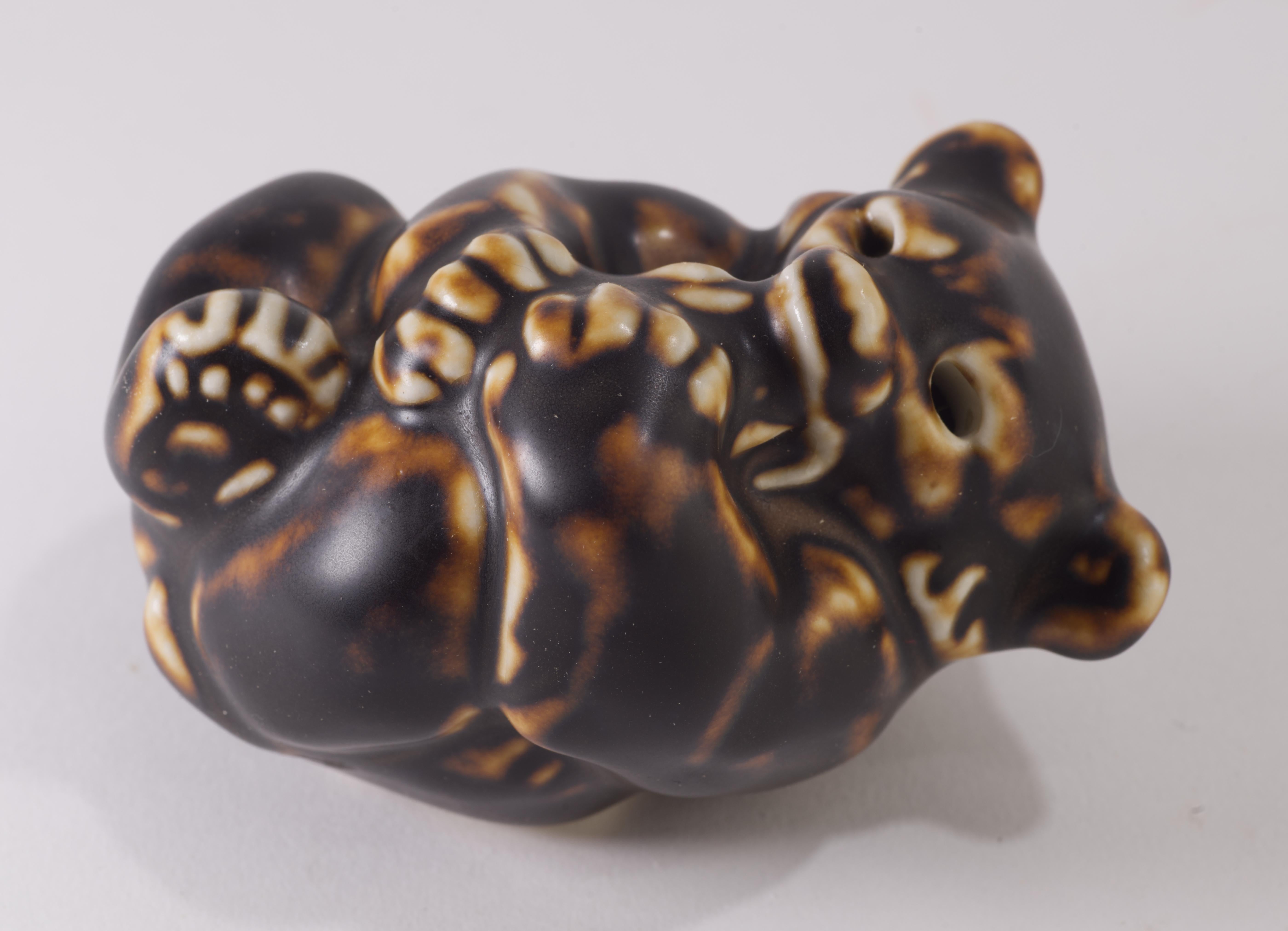  El bebé oso de porcelana fue diseñado por Knud Kyhn para Royal Copenhagen como parte de la serie creada en los años 1940-1950. El pequeño oso modelado está tumbado boca arriba acurrucado, con las patas recogidas, sosteniendo un juguete. El oso está