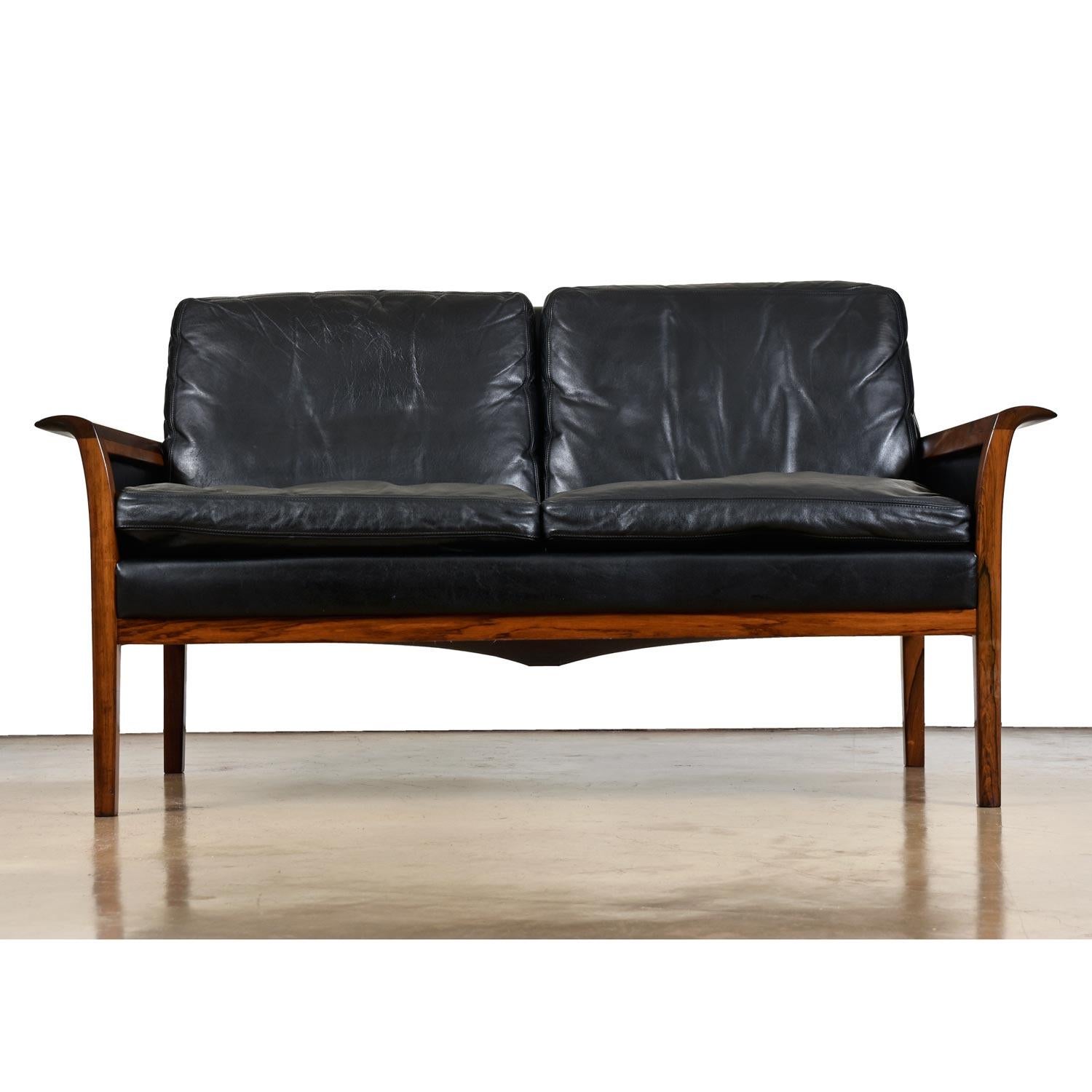 Two-seat loveseat sofa designed by Knut Saeter for Vatne Mobler. Solid rosewood frame with sculpted scroll armrests and original black leather. The Furnish Me VIntage team has not only restored this iconic sofa to excellent condition, but we