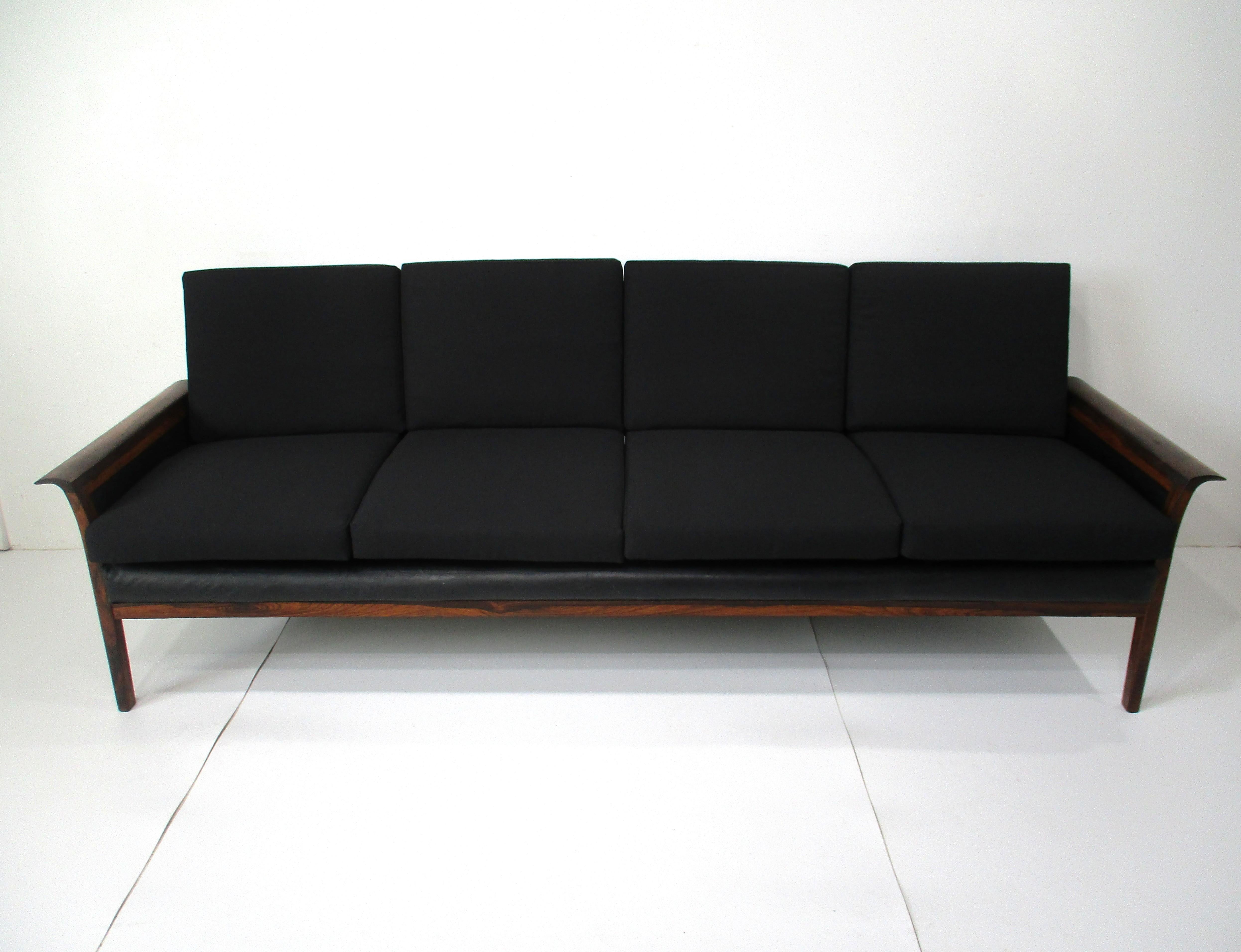 A dark Brazilian rosewood framed loose cushion sofa upholstered in black contract fabric with black leather sides and back . The winged semi rounded arms and contrasting materials give the piece a unique aesthetic that can work in any home interior