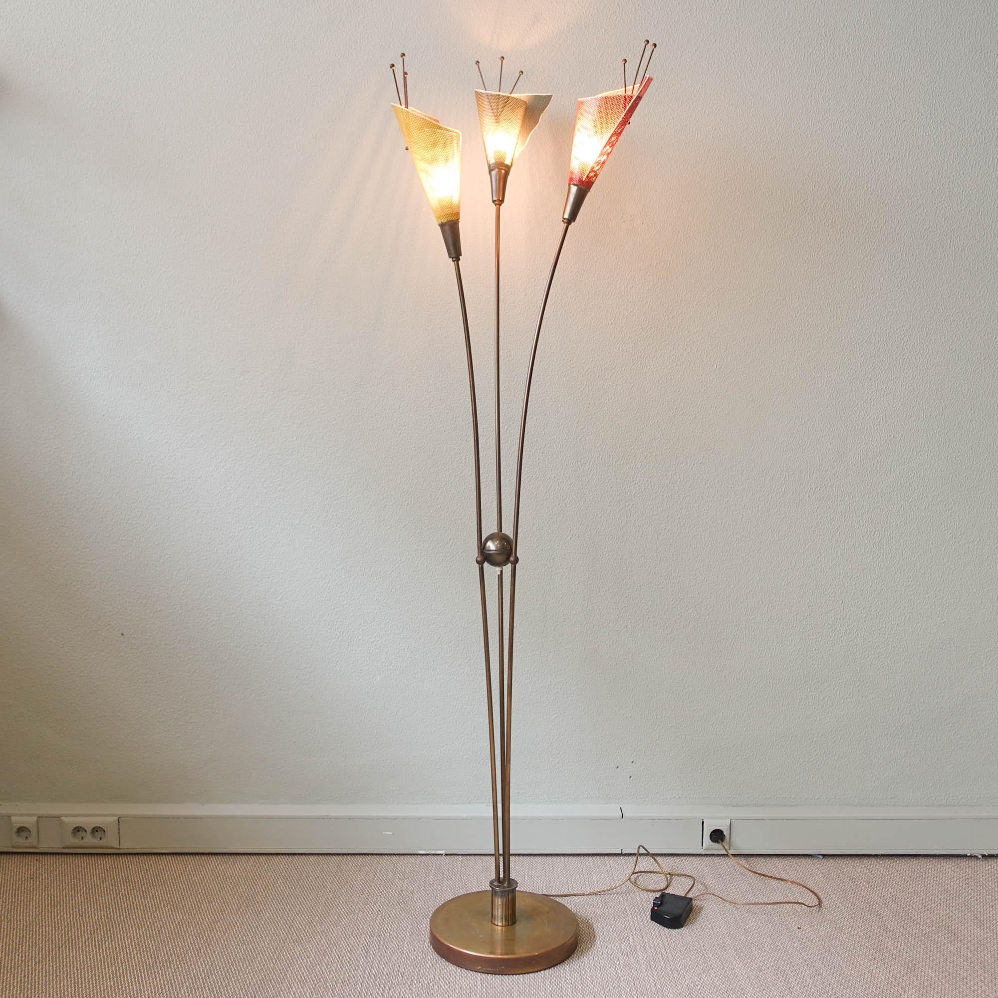 Ce lampadaire a été conçu et produit par Kobis & Lorne en France dans les années 1950. Il est composé de trois abat-jour métalliques perforés, de couleur rouge, verte et jaune, en forme de fleur, qui sont fixés à un bras en laiton. Avec un design