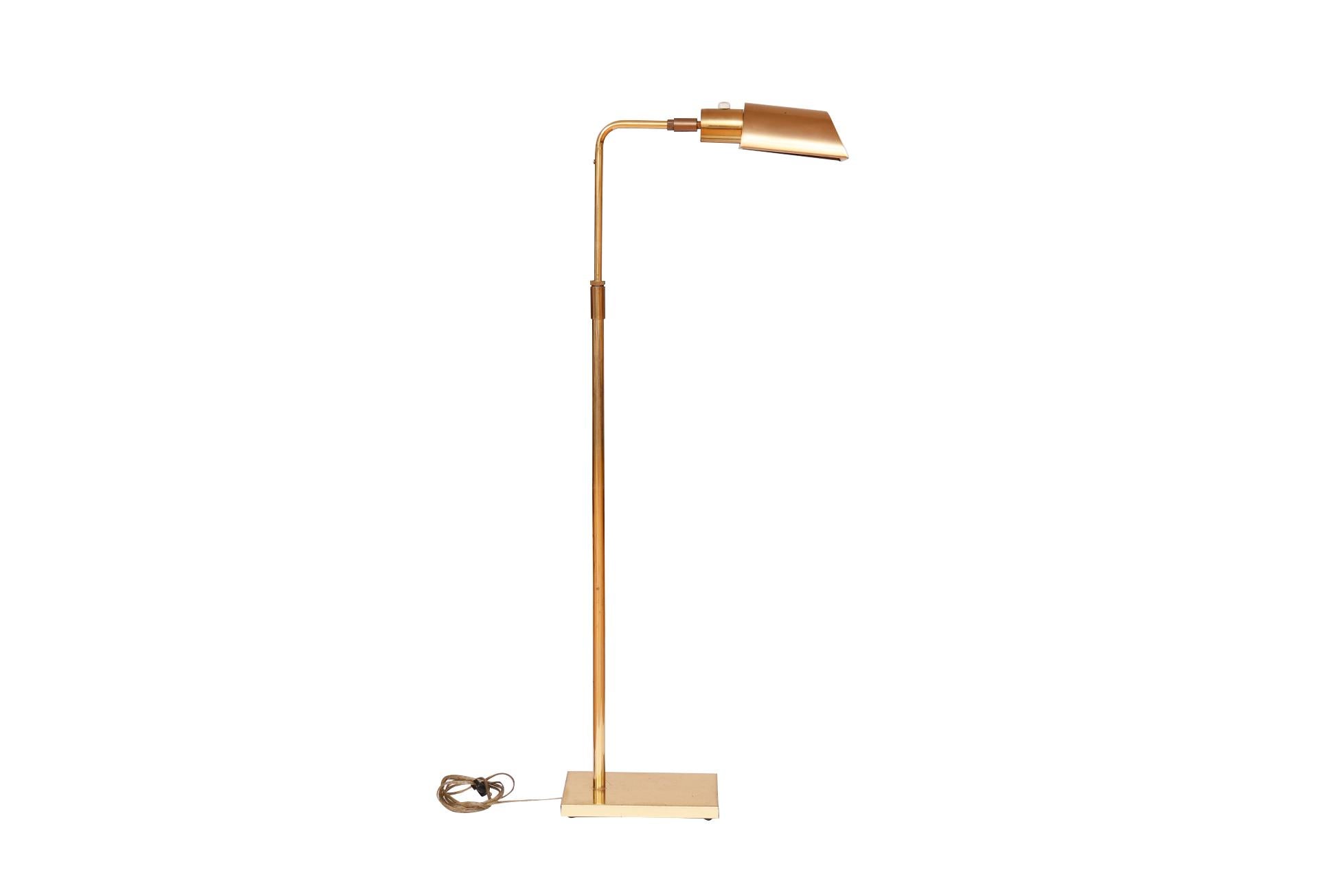 A 1960's Mid-Century Modern adjustable pharmacy floor lamp in brass, made by Koch + Lowy. A half cylindrical shaped brass shade can be angled up or down and rotates on a brass column which can also be raised or lowered. Stands on a sleek weighted