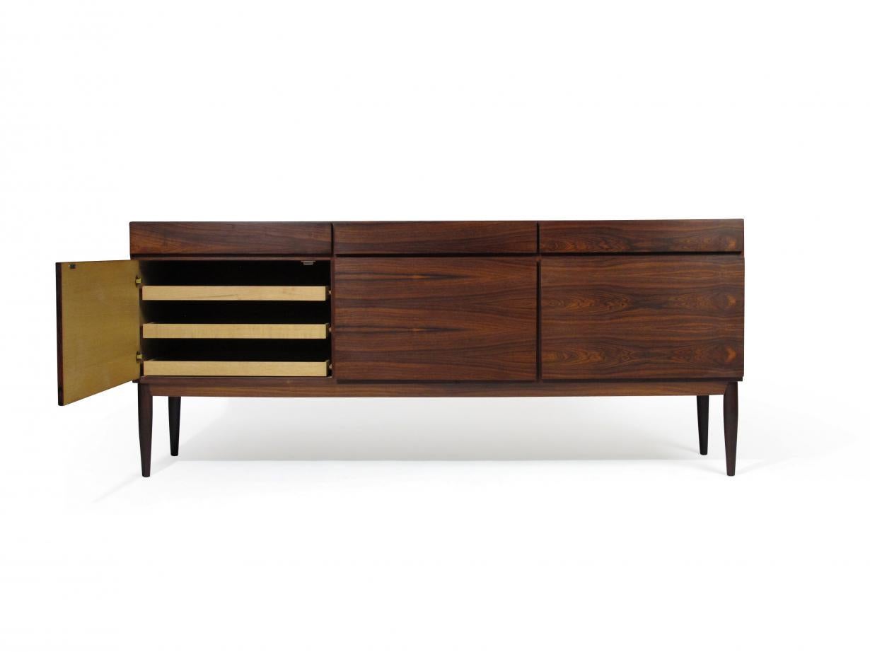 Rosewood sideboard designed by IB Kofod Larsen for Faarup Moblefabrik crafted of rosewood three bays of doors with stunning book-match grain across front. White oak interior with adjustable shelves, and series of silverware drawers, raised on solid