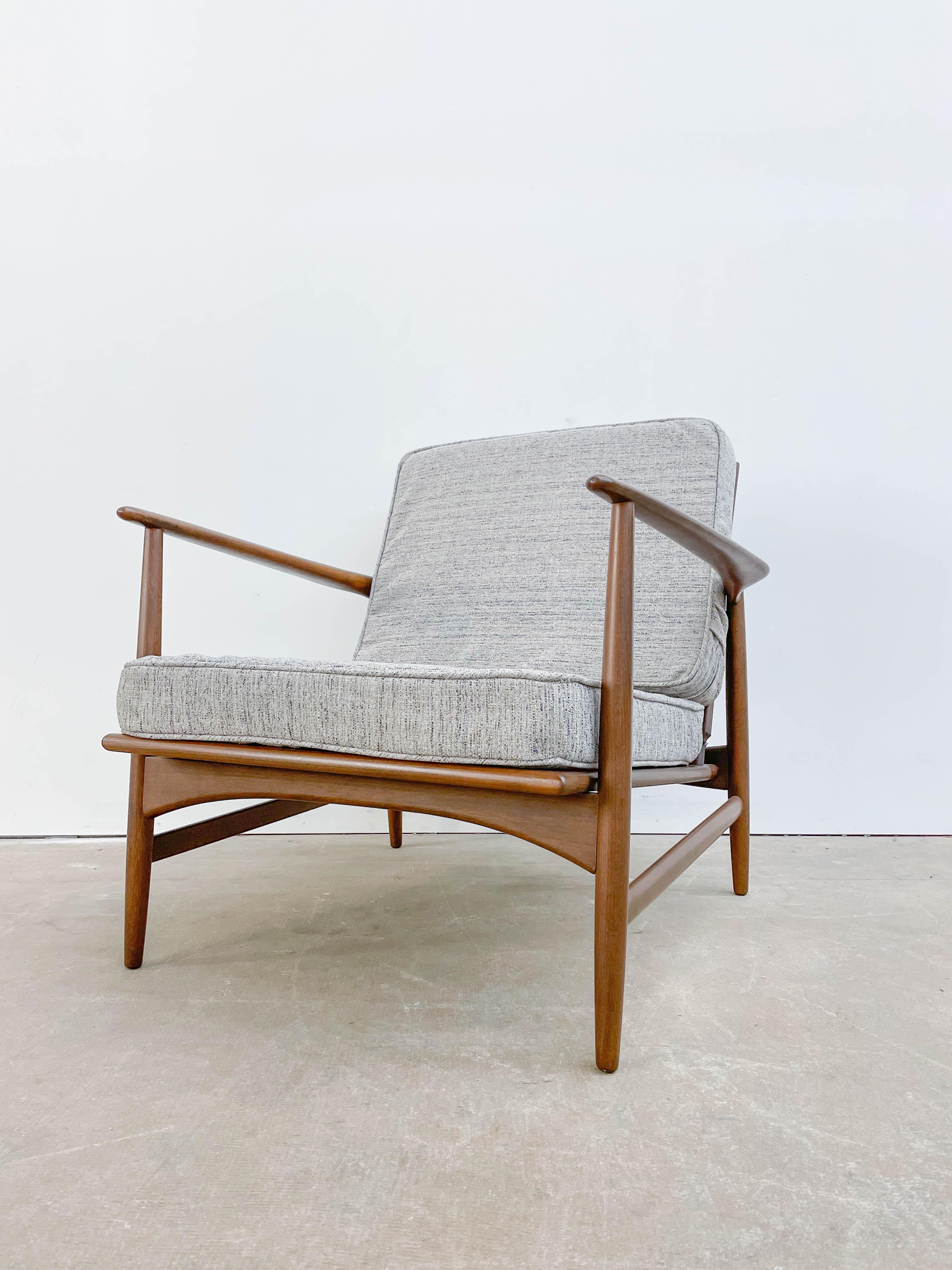 This attractive Danish Modern lounge chair was designed by Ib Kofod Larsen for Selig in the 1960s. It boasts a sleek and ergonomic design that looks great from every angle. The lounge chair has a solid beech frame with walnut tone finish, which