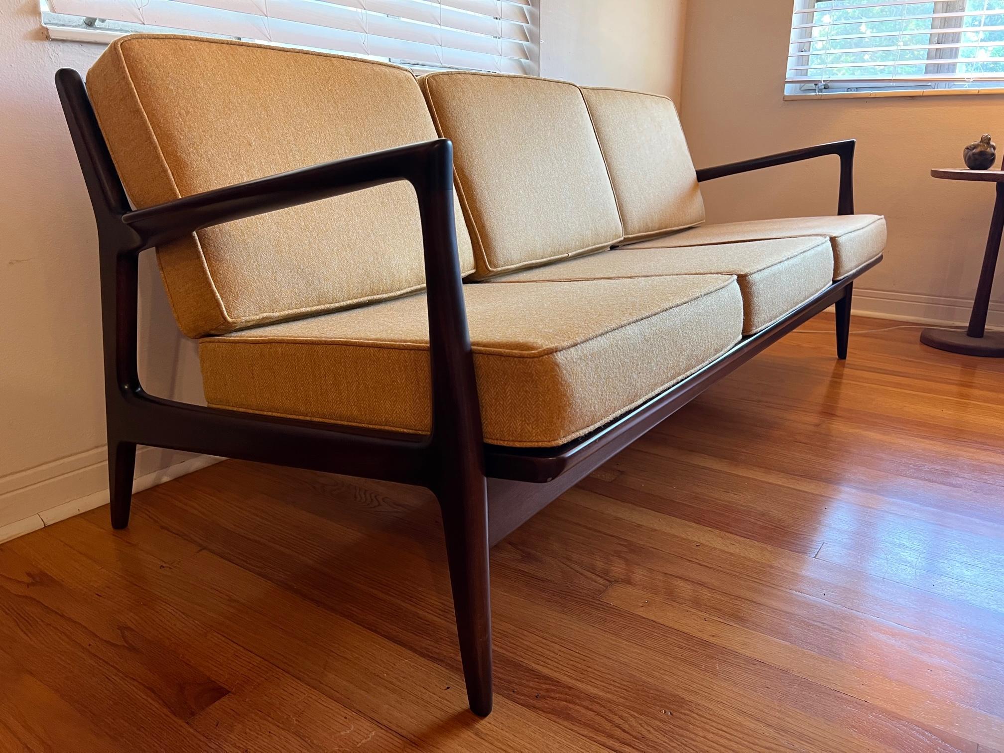 A classic three seat sofa designed by IB Kofod Larsen, manufactured in Denmark and distributed through Selig. Frames restored, new straps, reupholstered in British ochre colored tweed (100% wool content). 
