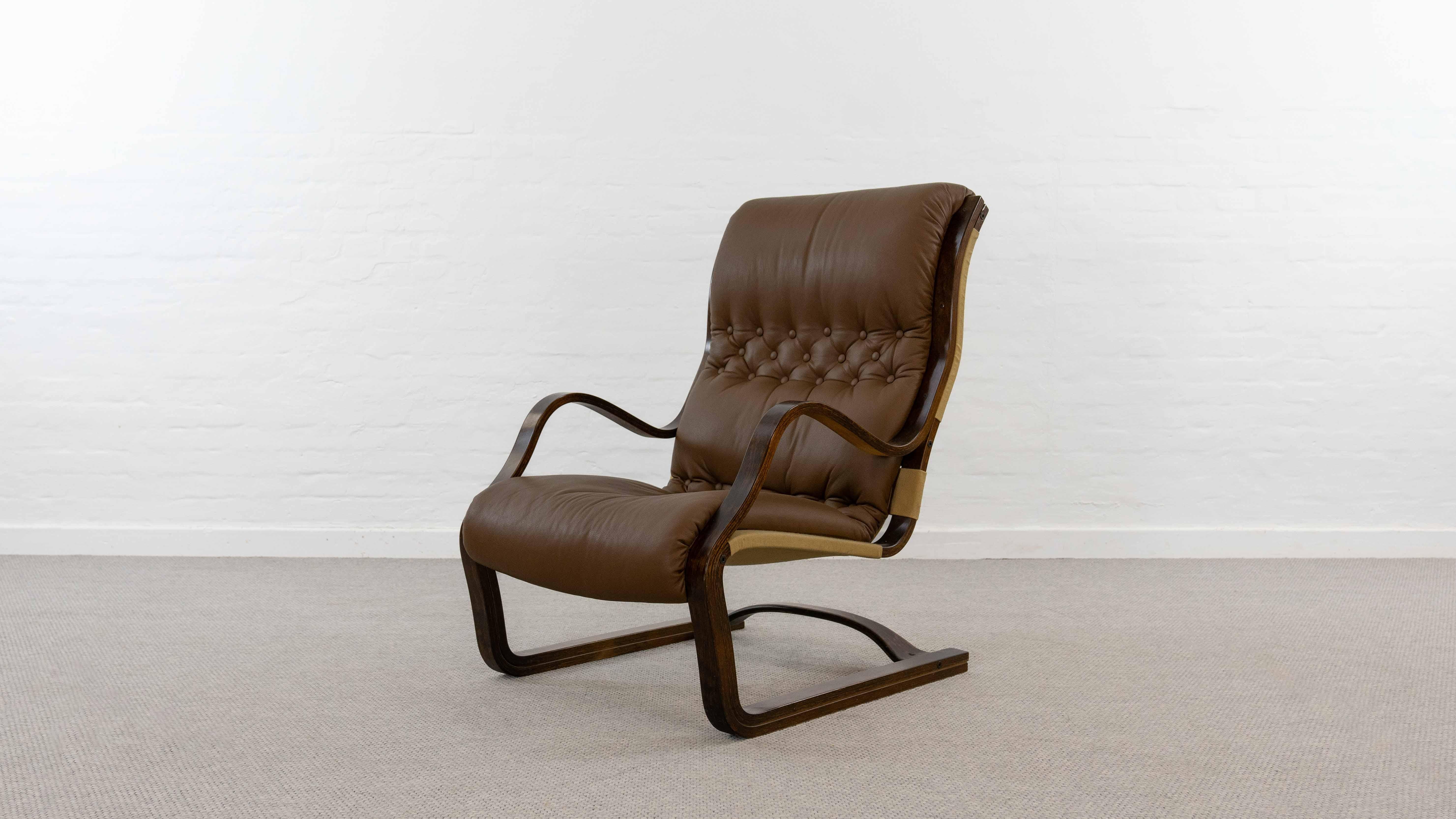 Koivutaru freepending easy chair. Designed 1977 by Esko Pajamies for Asko, Finland. Upholstered in its original brown buttoned leather. The perfect fireplace chair. Very nice bent wood forming of the armrests and the chairbase. Stained birchwood –