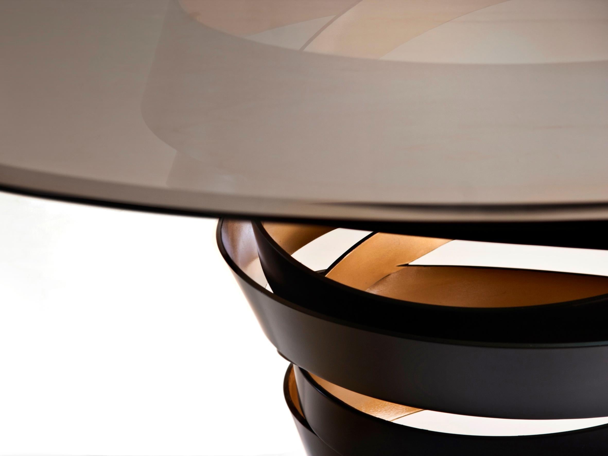 The swirling metal ribbon of the Intuition dining table evokes the mysterious and divine feminine instinct. Carefree and unexpected swirls are guided by emotions and desires. The two-tone metal base is topped with a perfect glass circle top. Without
