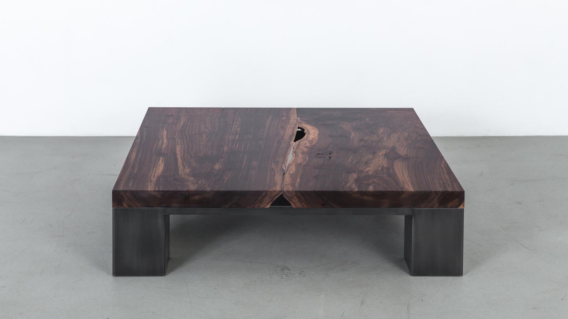 La table basse Kong est créée à partir d'un plateau en bois massif en finition noyer:: posé sur un cadre en acier. L'équilibre visuel de sa forme et de son poids crée un contraste dynamique avec le détail du bord organique vers le centre du plateau