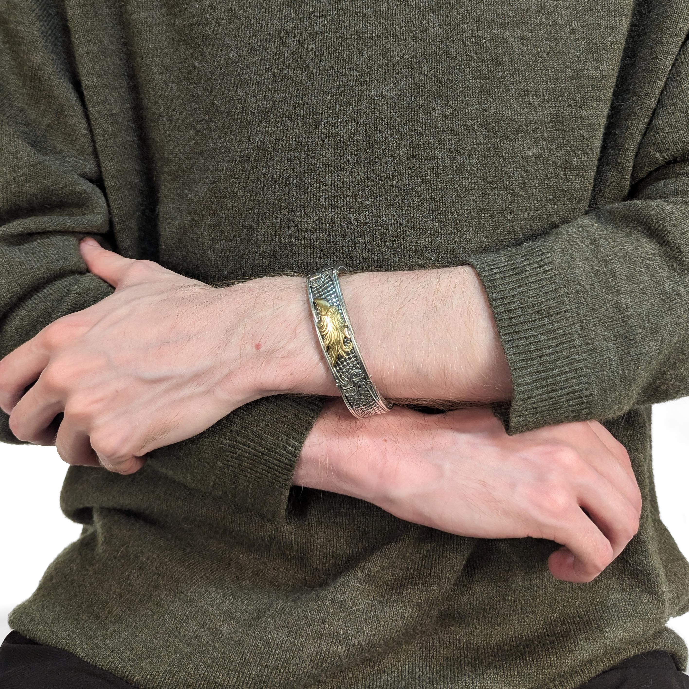 Un raffinato bracciale greco firmato in argento e oro.

Da Konstantino.

Dalla serie Heonos.

In argento sterling con una testa d'aquila in oro giallo 18 carati in rilievo. L'argento è inciso e sbalzato con ali d'aquila e dispositivi
