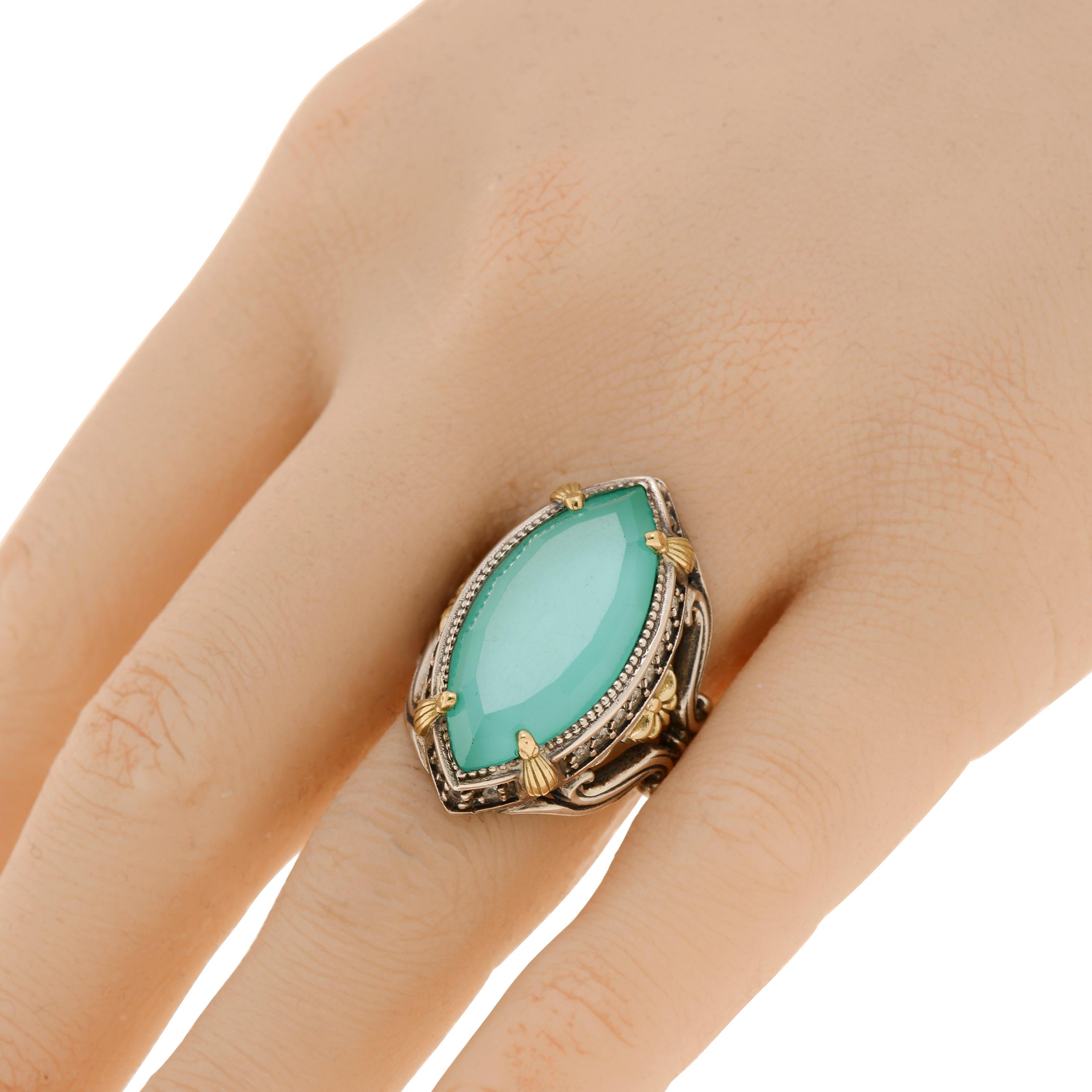 This eye-catching Konstantino ring features a teal chalcedony doublet center with white topaz, set in sterling silver with 18K yellow gold accents. The decoration size is 15/8” x 1 1/8”. The weight is 15g. The ring size is 6.75 (53.8).
