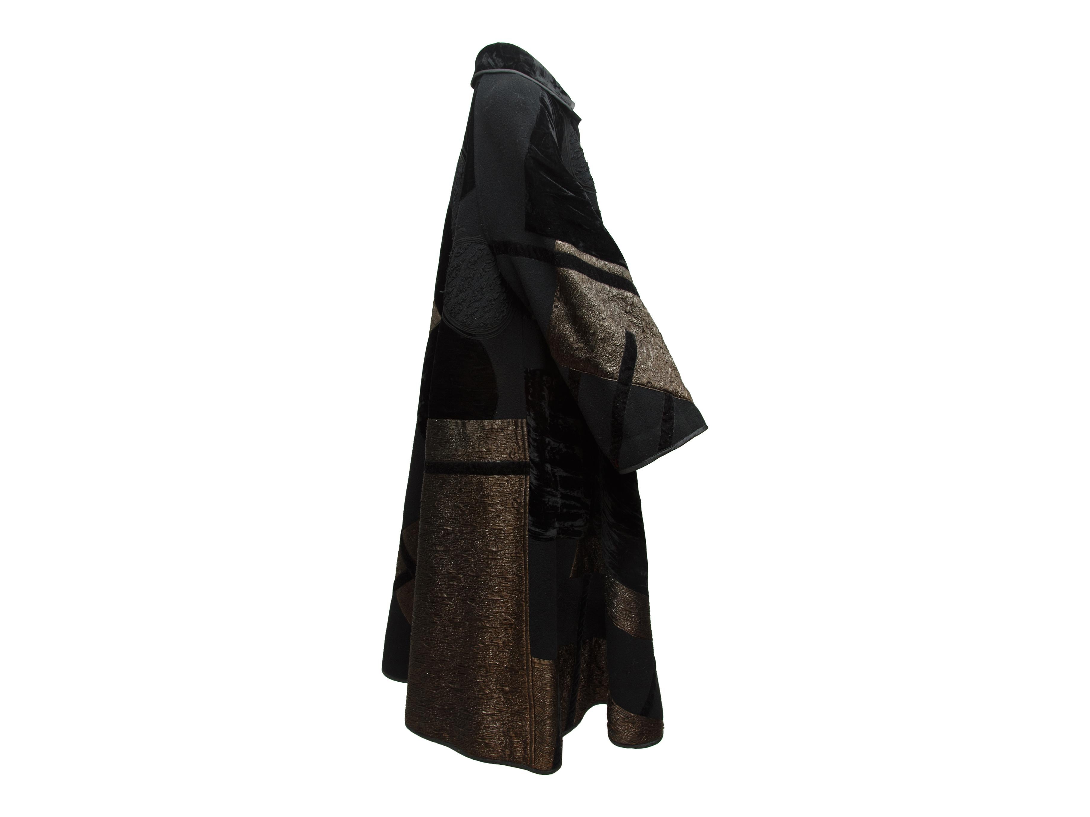 Product details: Black velvet long coat by Koos Van Den Akker Couture. Metallic brocade and velvet abstract pattern throughout. Pointed collar. Button closures at front. 40