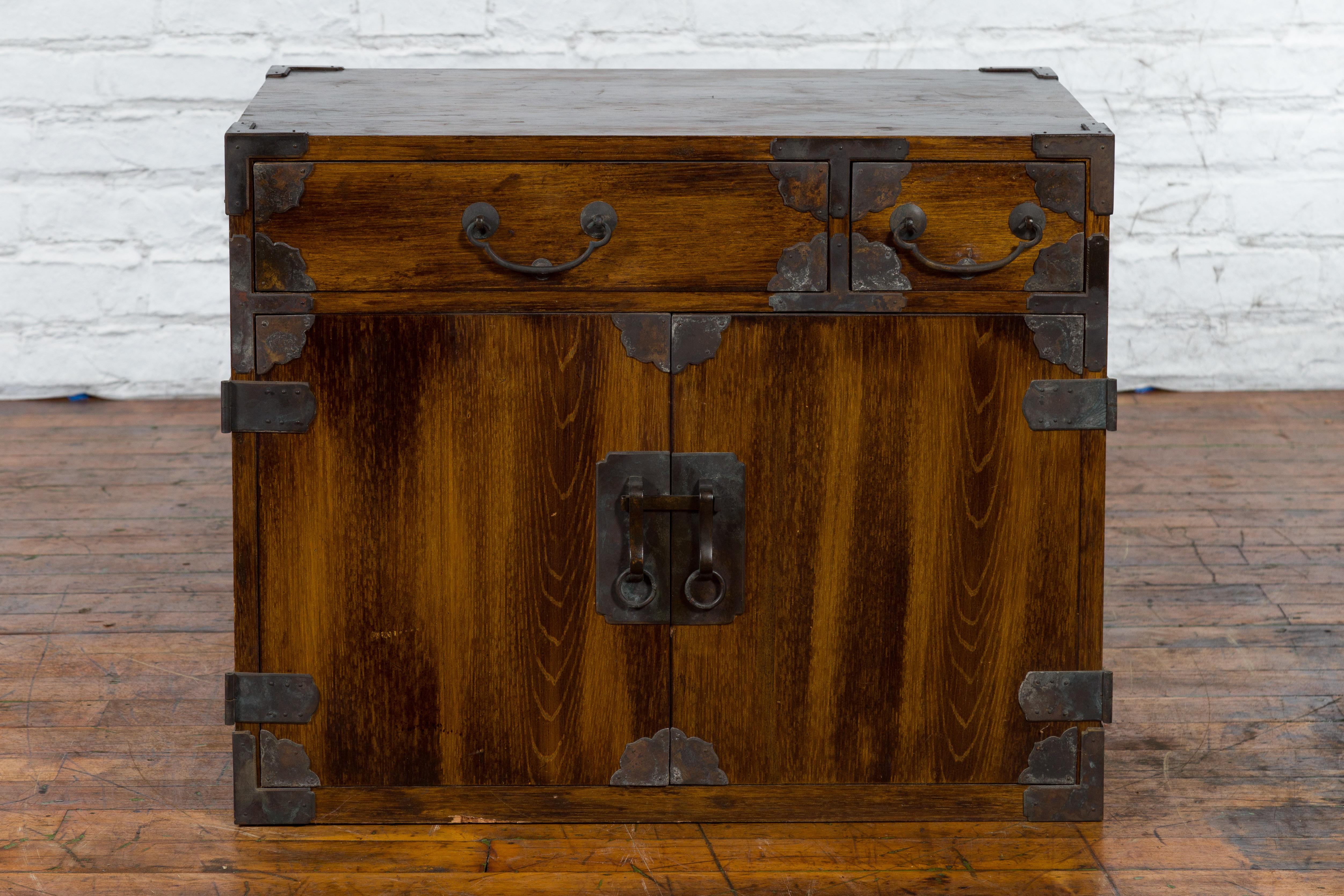 An antique Korean brown wood side cabinet from the 19th century with iron hardware, drawers, and doors. Created in Korea during the 19th century, this wooden side cabinet features a linear silhouette perfectly complimented by an abundant iron