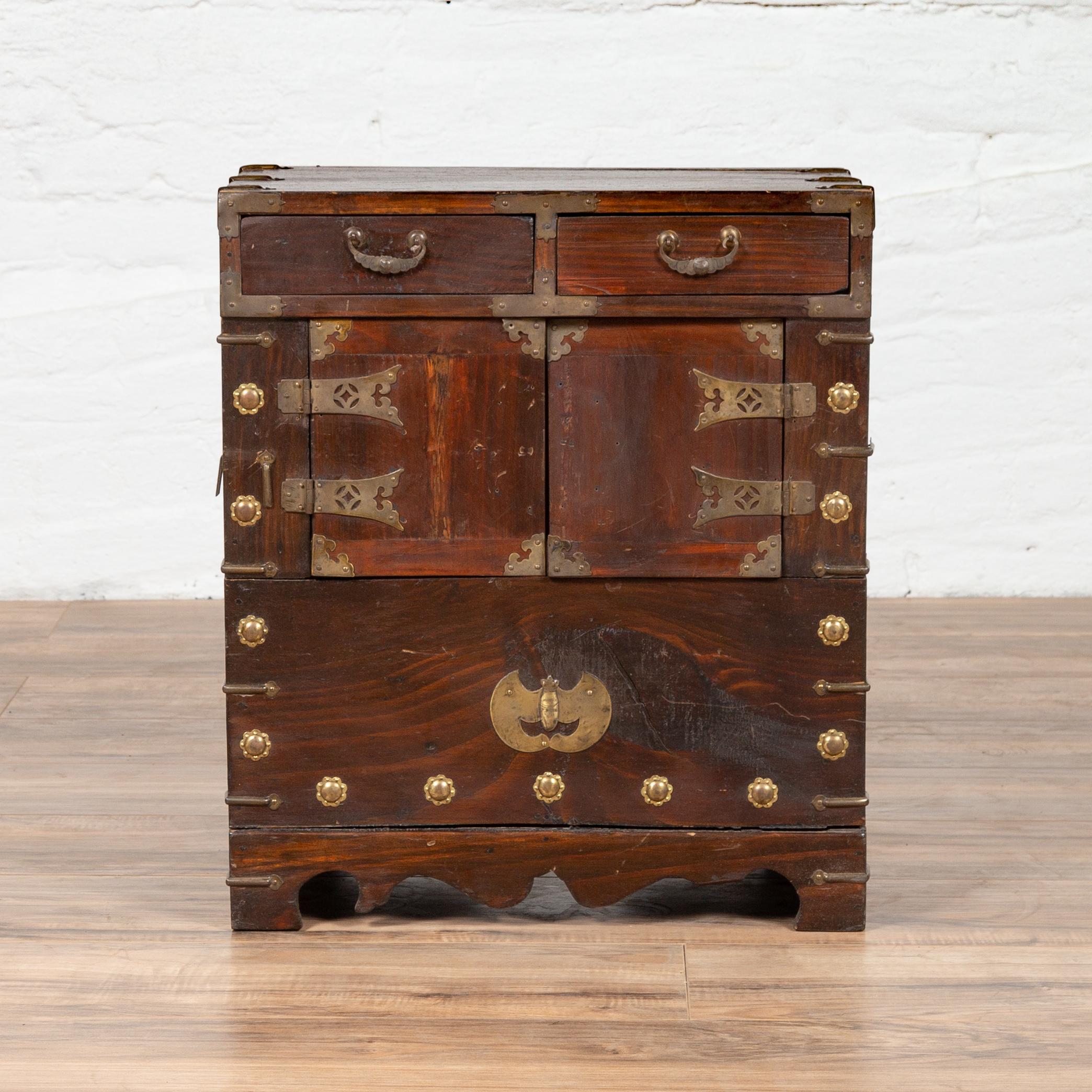 A Korean vintage side chest with two drawers, double doors and brushed brass hardware. This small Korean cabinet features a rectangular top with brass braces on the sides, resting above two upper drawers, each fitted with a bail handle. A pair of