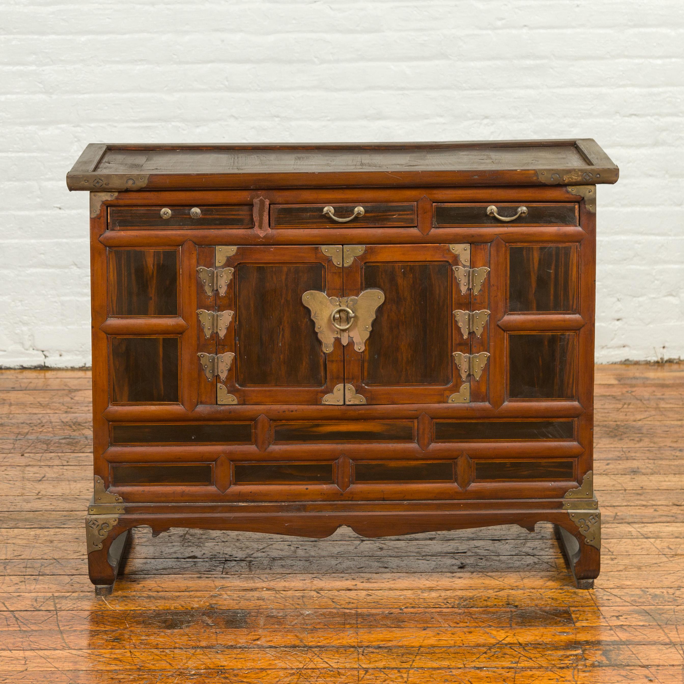 An antique Korean cabinet from the 19th century, with three drawers, double doors, brass butterfly hardware and horsehoof feet. Born in Korea during the 19th century, this wooden cabinet features a rectangular top with slightly recessed central