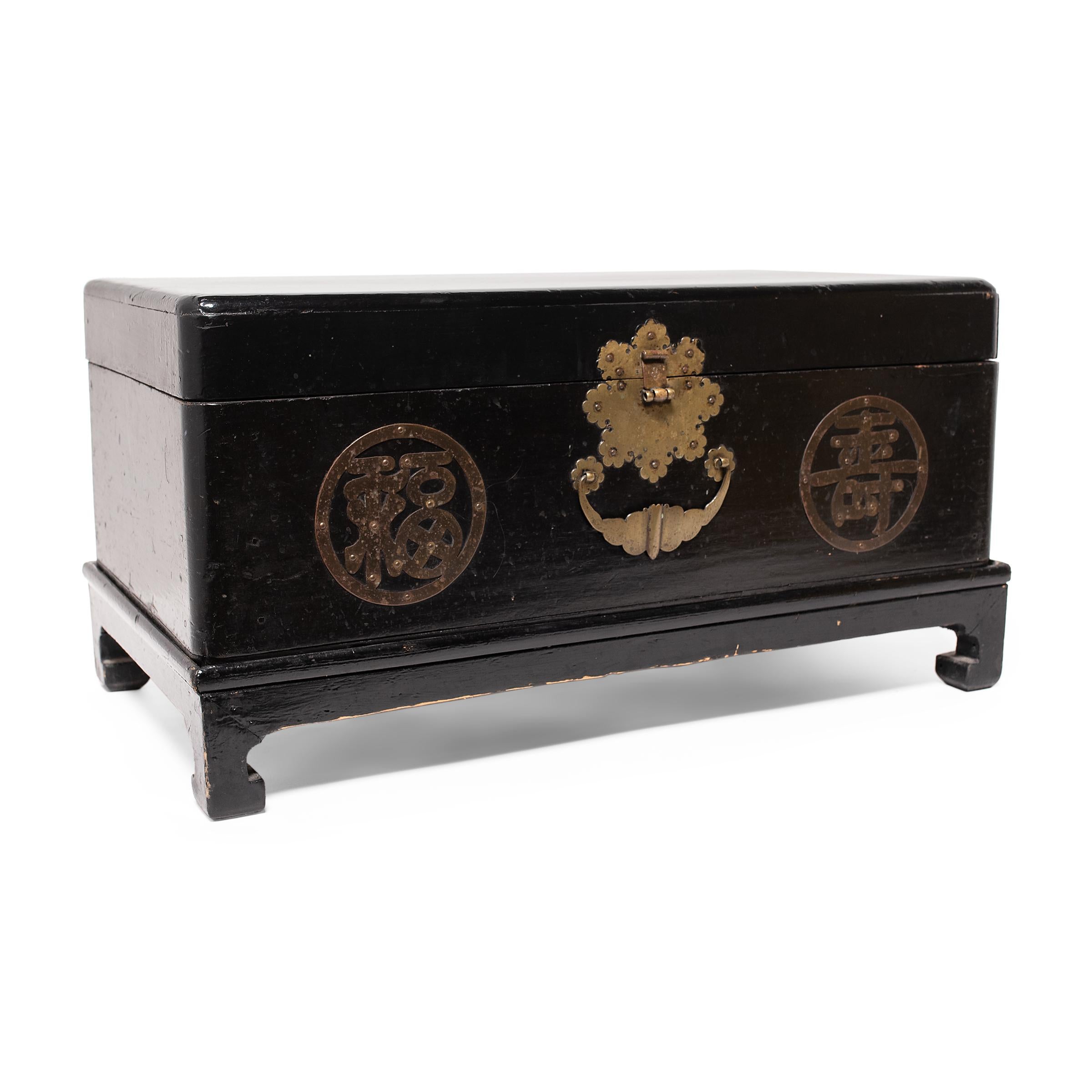 This low Korean wedding chest is cloaked in an all-over black lacquer finish, punctuated by decorative brass hardware on the front. Enclosed within round medallions, two brass characters offer blessings of luck (福) and longevity (寿). The lock plate
