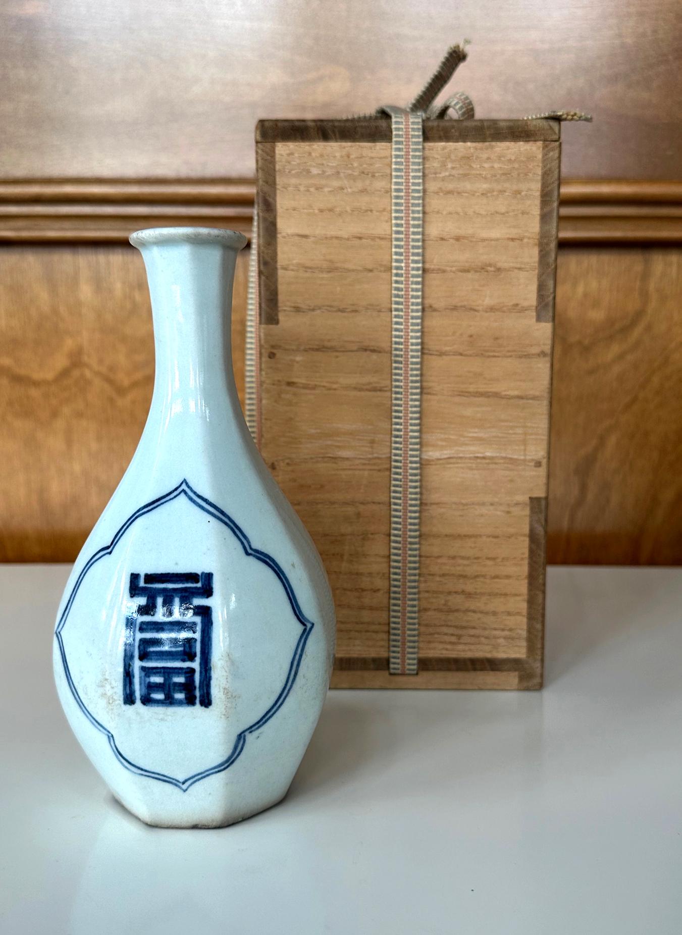 A Korean blue and white long neck vase in bottle form with octagonal faceted surface from Joseon Dynasty (19th century). The elegant vase is covered in a white glaze with a tint of celadon blue. It prominently features two large archaic-form Hanja