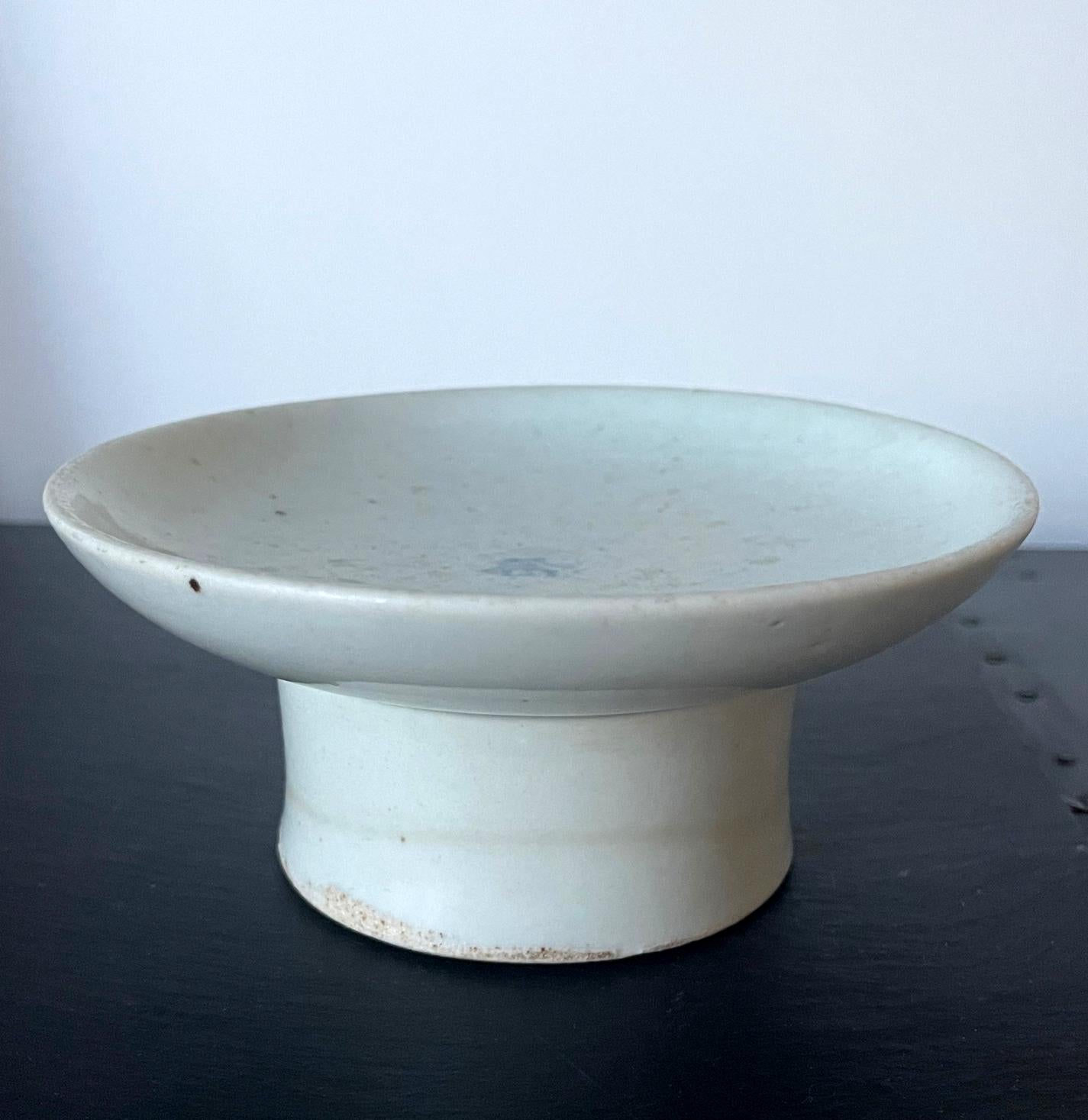 A small ceramic stemmed dish with high cylindrical foot in white glaze with a cobalt blue underglaze inscription in the center from Korea, circa 18-19th century Joseon Dynasty. This is a classic ceremonial vessel that was used to offer the sweet